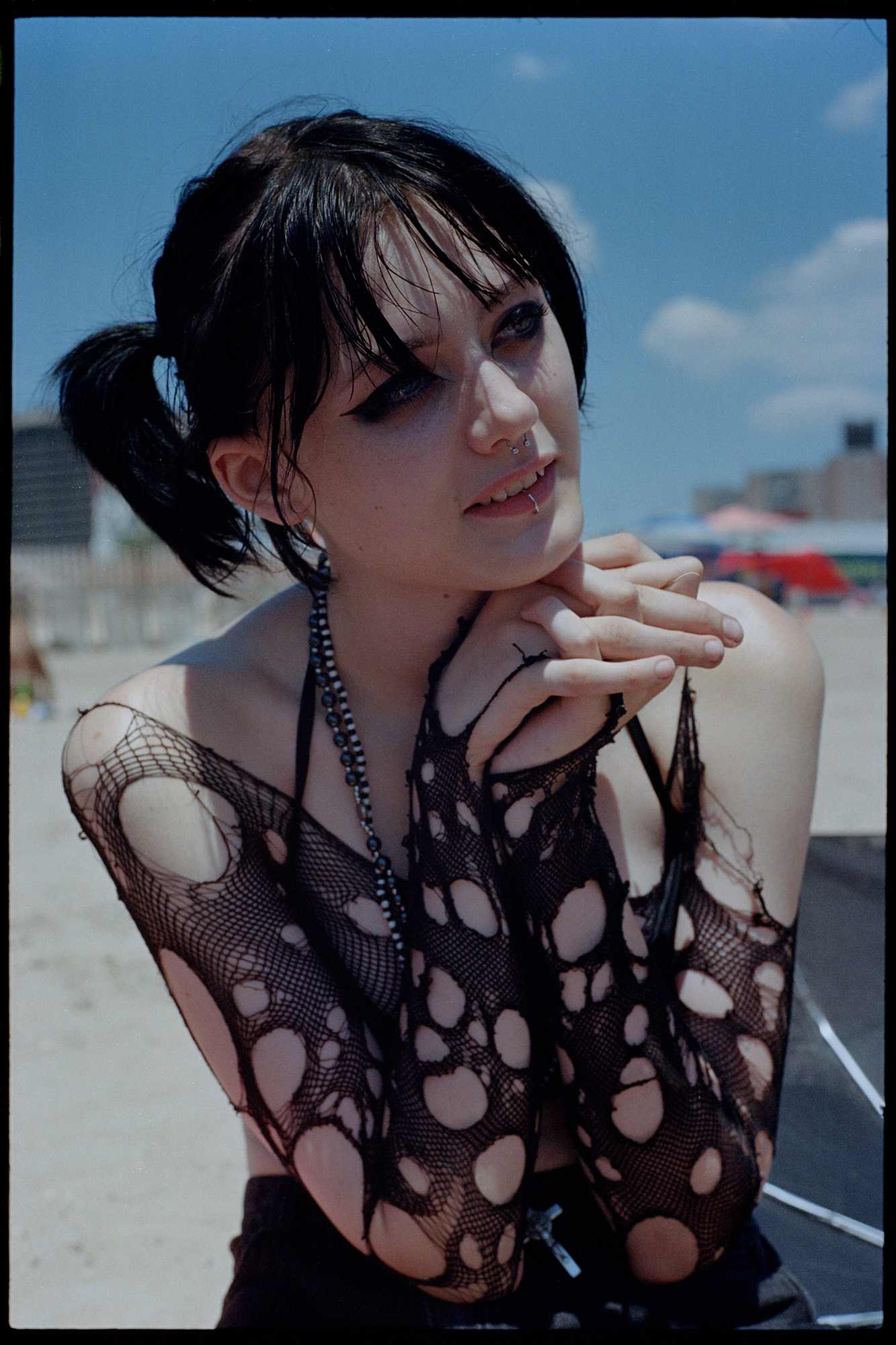 a teenager in a torn fish net top, facial piercings and hair in pigtails looks off camera.