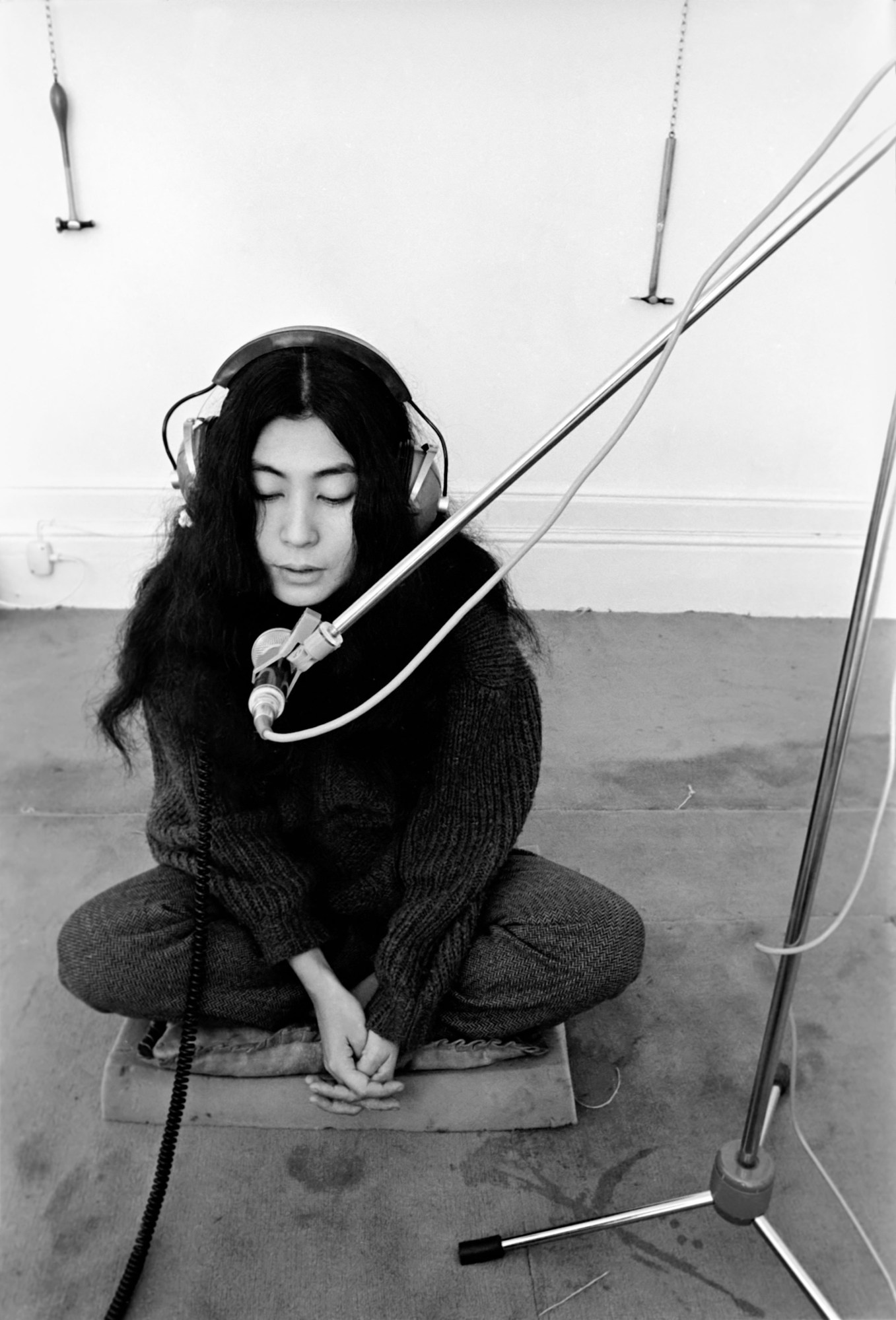 a young yoko ono sits cross-legged on a block of foam; she has headphones on and is recording vocals