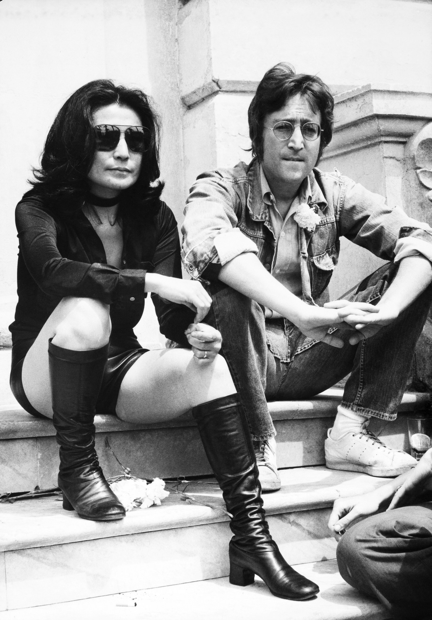 john lennon and yoko ono sitting on steps wearing sunglasses, with flowers at their feet