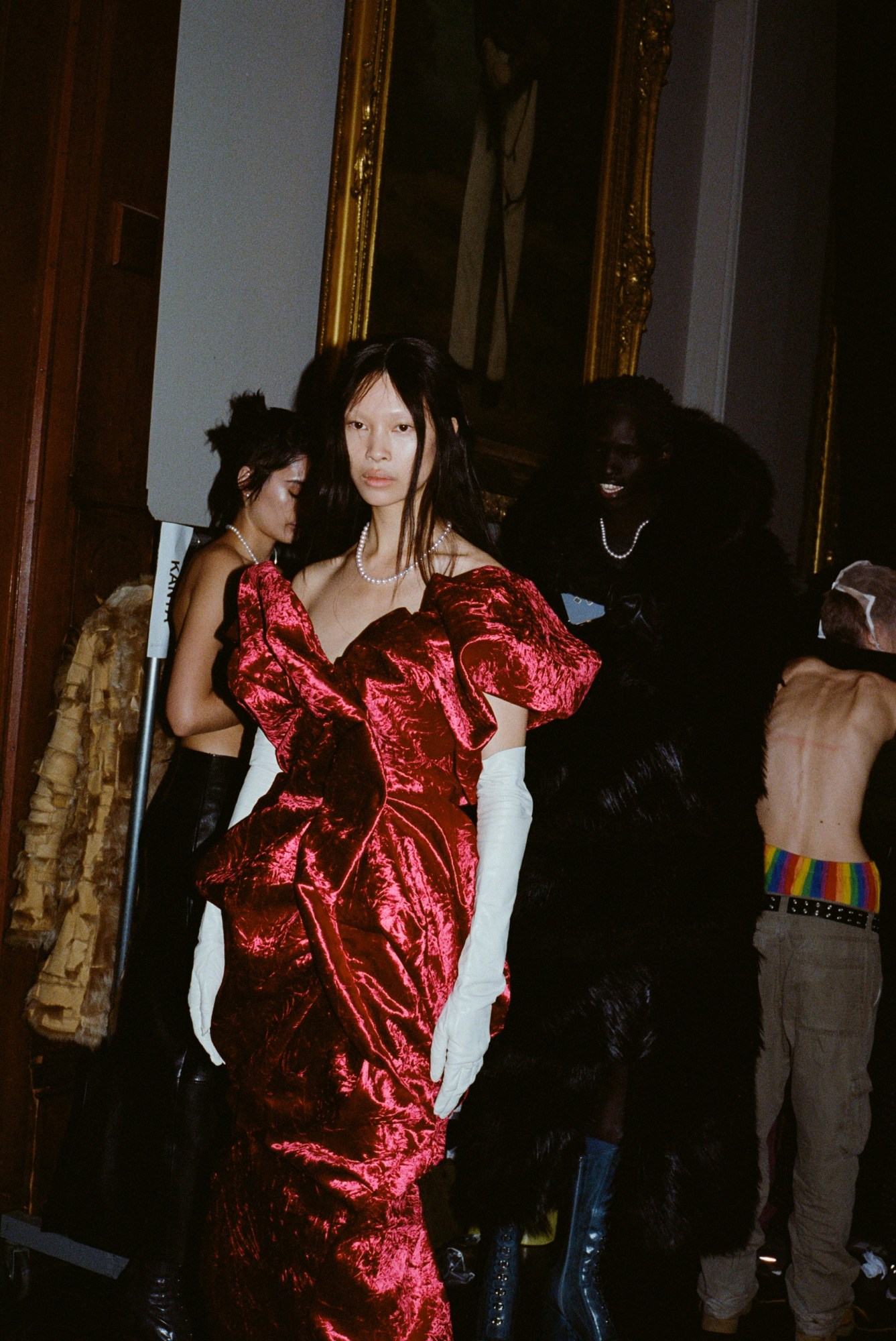 a woman in a red ballgown waits backstage at marc jacobs aw23