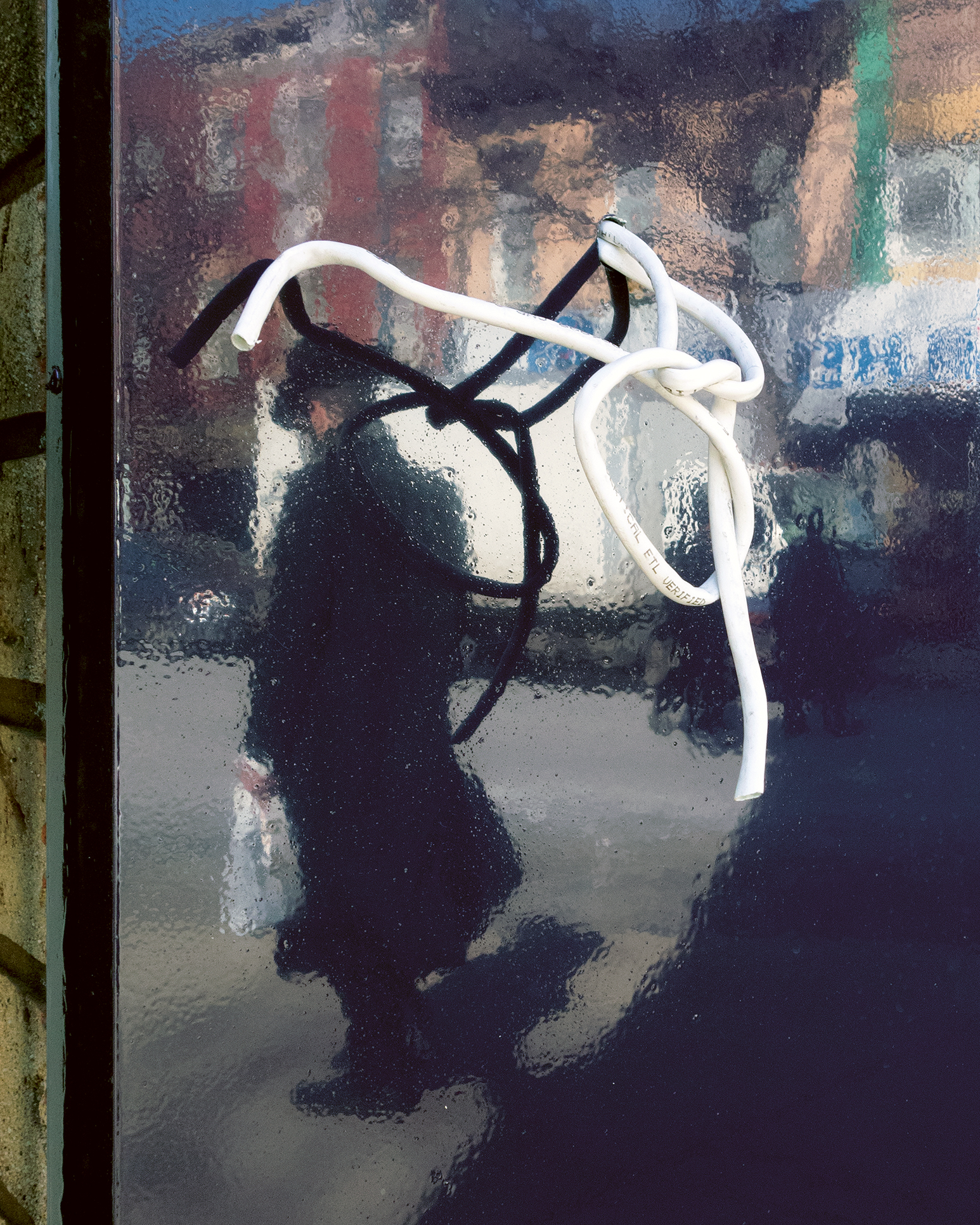 a rope comes through a mirrored surface. in it, a rough outline of a hasidic jew is seen