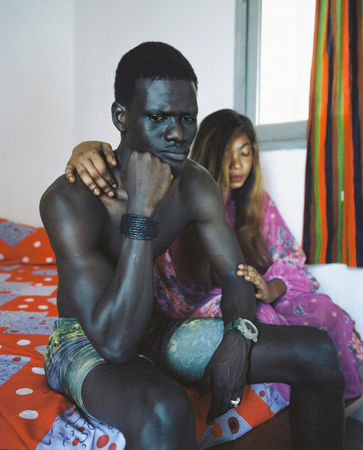 a sengalese couple sitting pensively on their bed