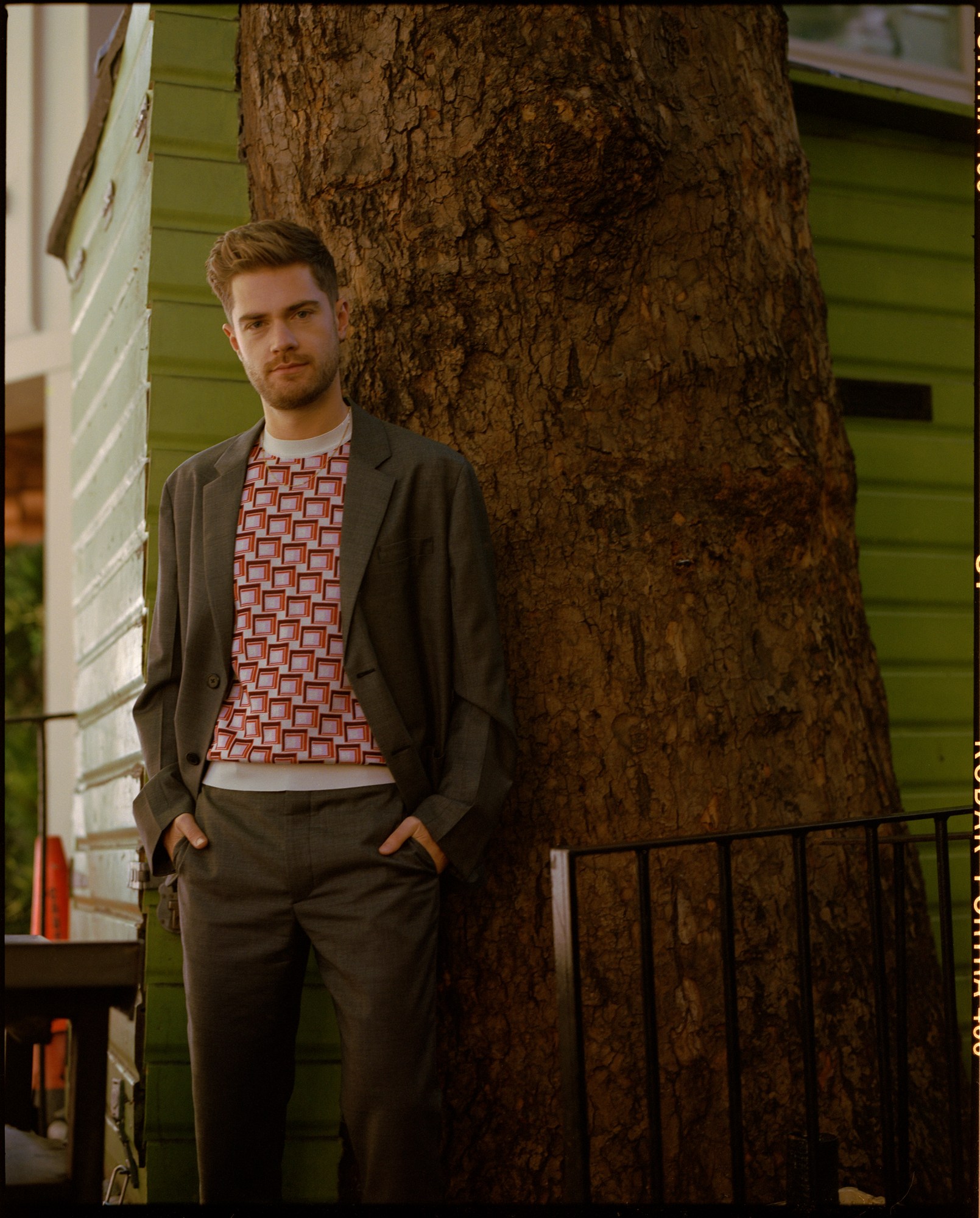 lukas dhont, a male film director, looks to the camera in a full-length photo, a tree is behind him.