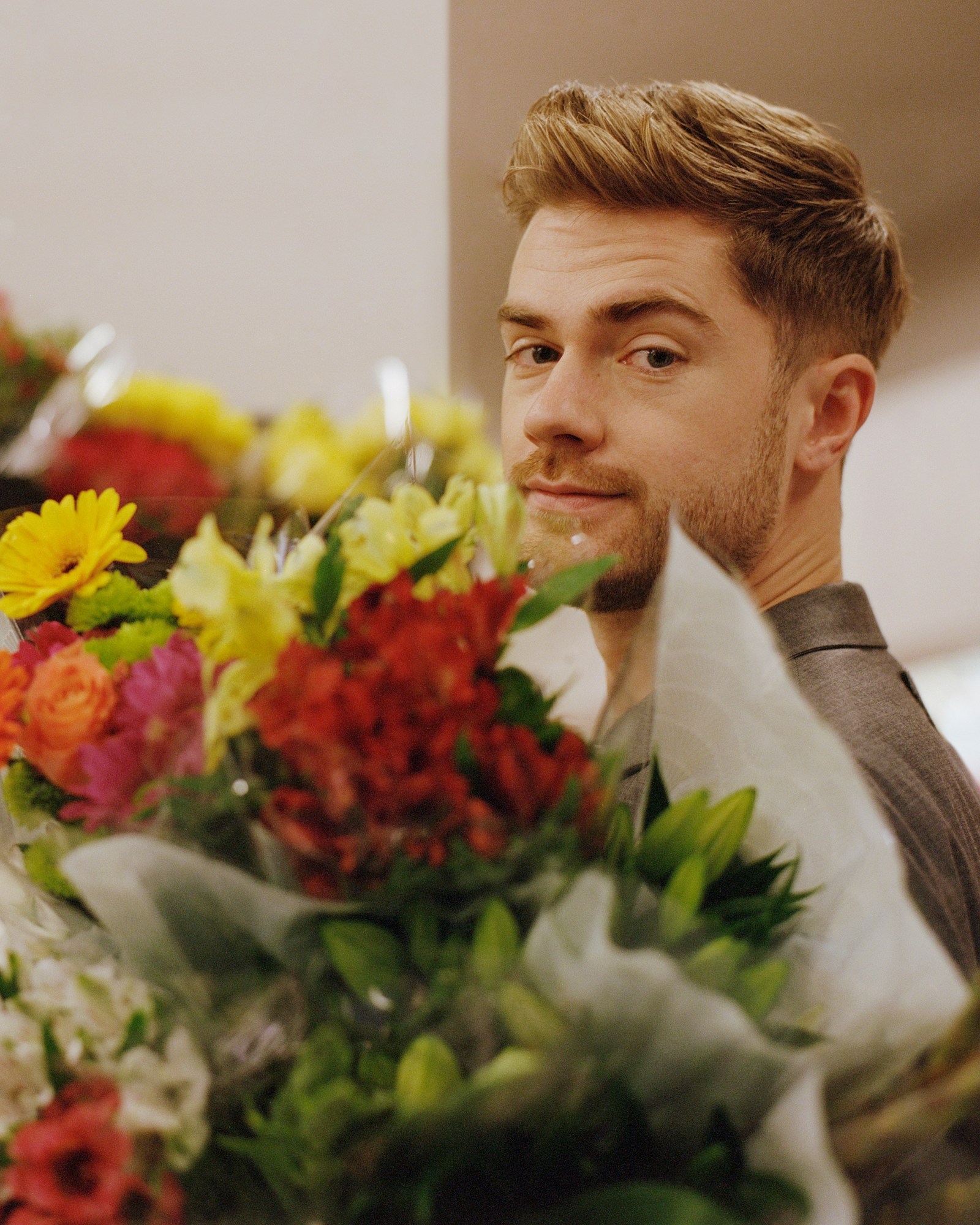 a photo of director lukas dhont looking over a bunch of flowers into the camera