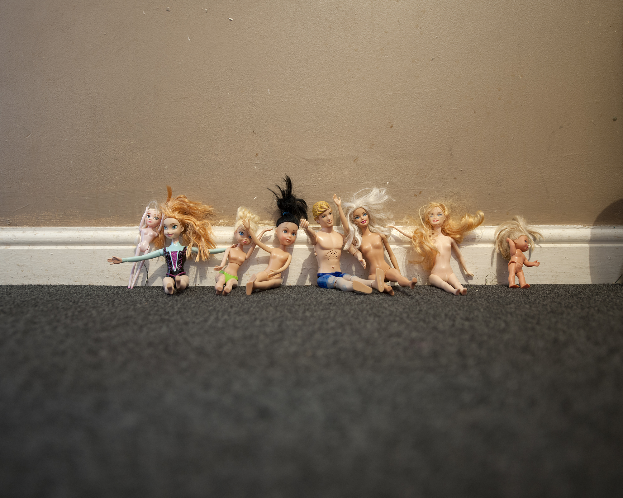 a group of mostly naked barbies with messy hair are lined up against a skirting board