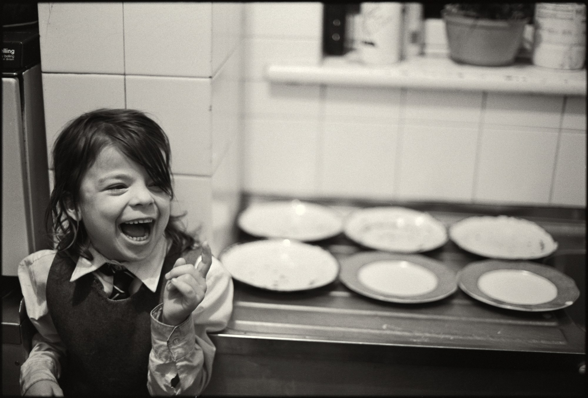 a young child in school uniform laughs beside a sideboard of empty dinner plates