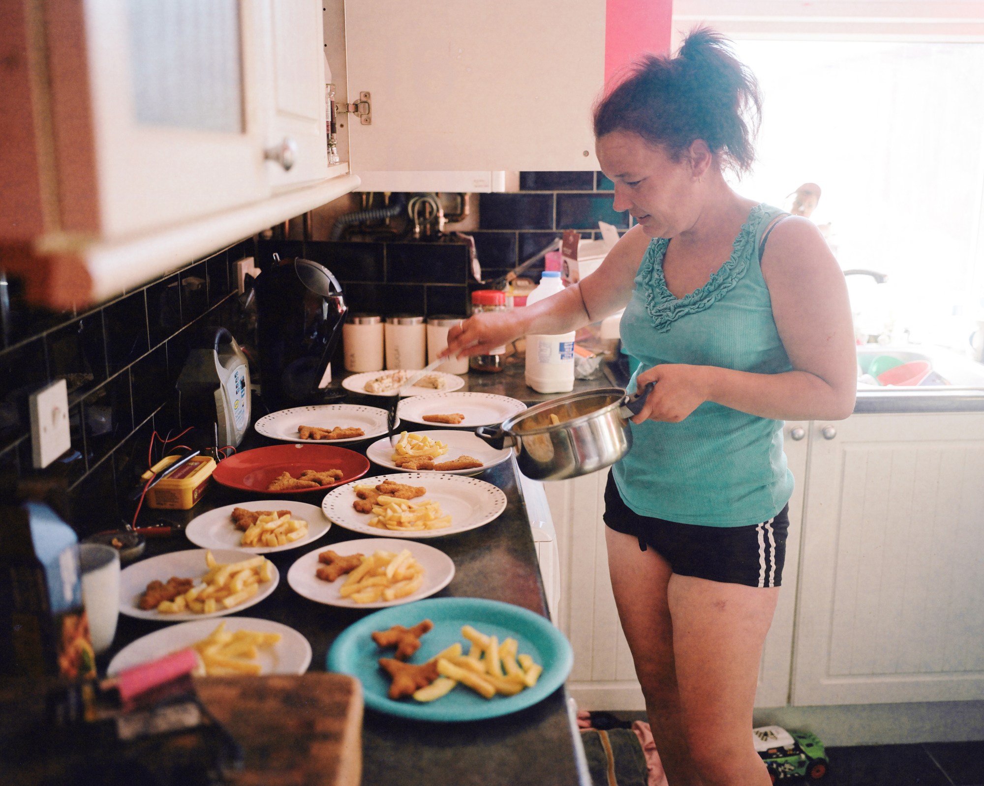 a woman in shorts and a vest top plates up 11 meals of nuggets and chips in a family kitchen