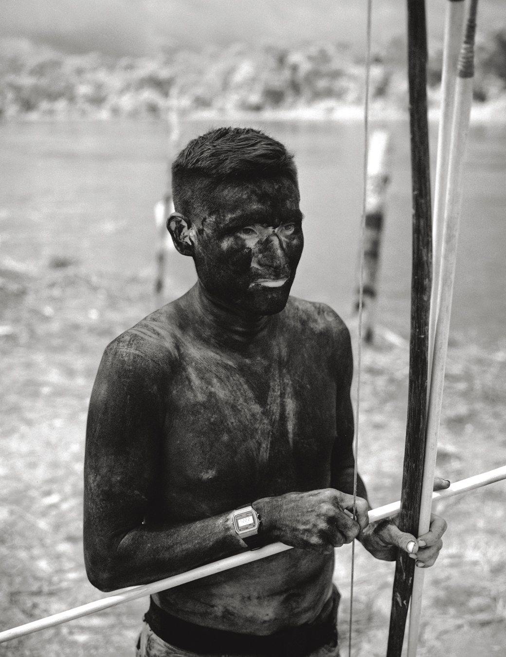 Photograph from Richard Mosse's immersive video artwork Broken Spectre of a boy covered in mud and holding a tool