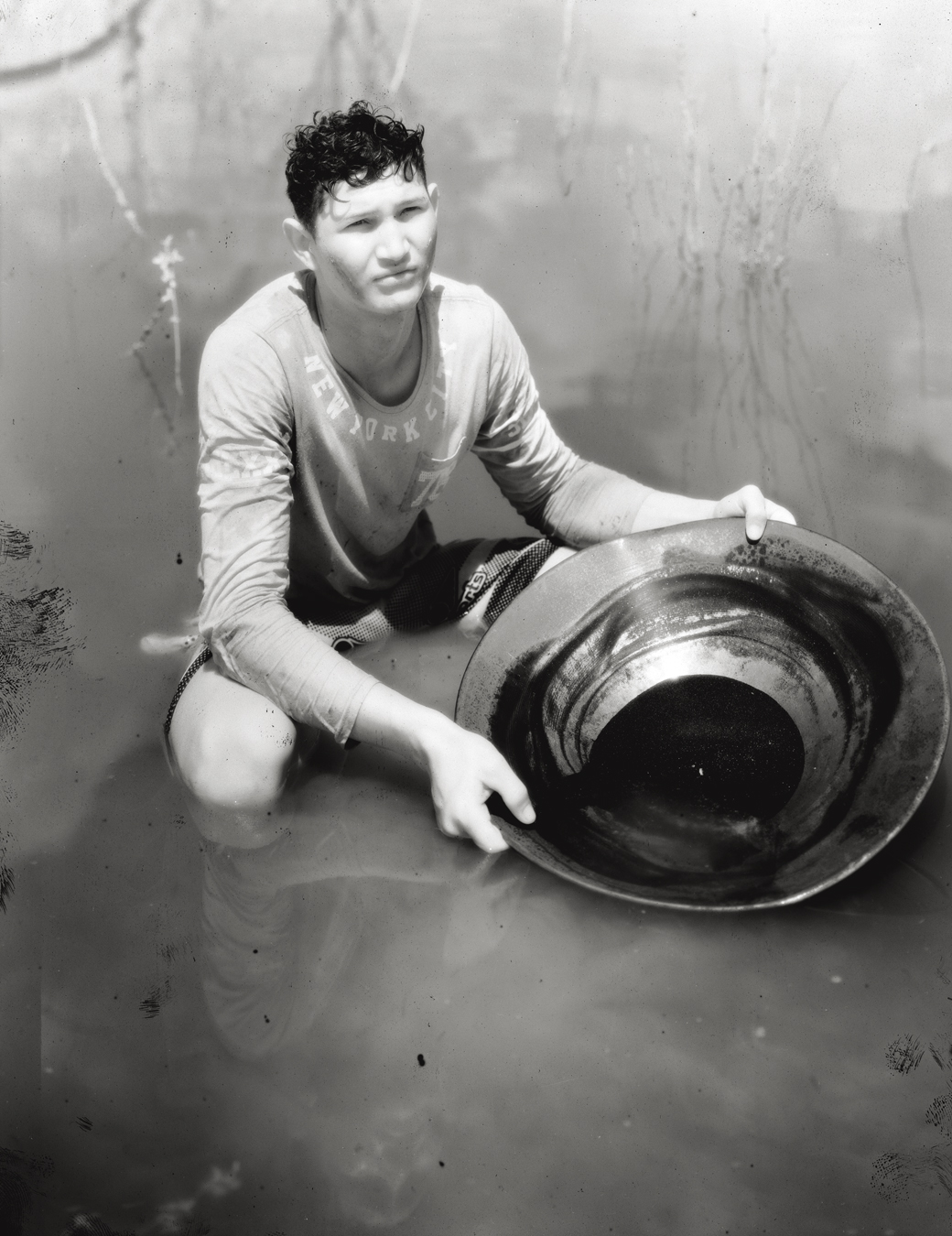 Photograph from Richard Mosse's immersive video artwork Broken Spectre of a boy holdin a pan in the river