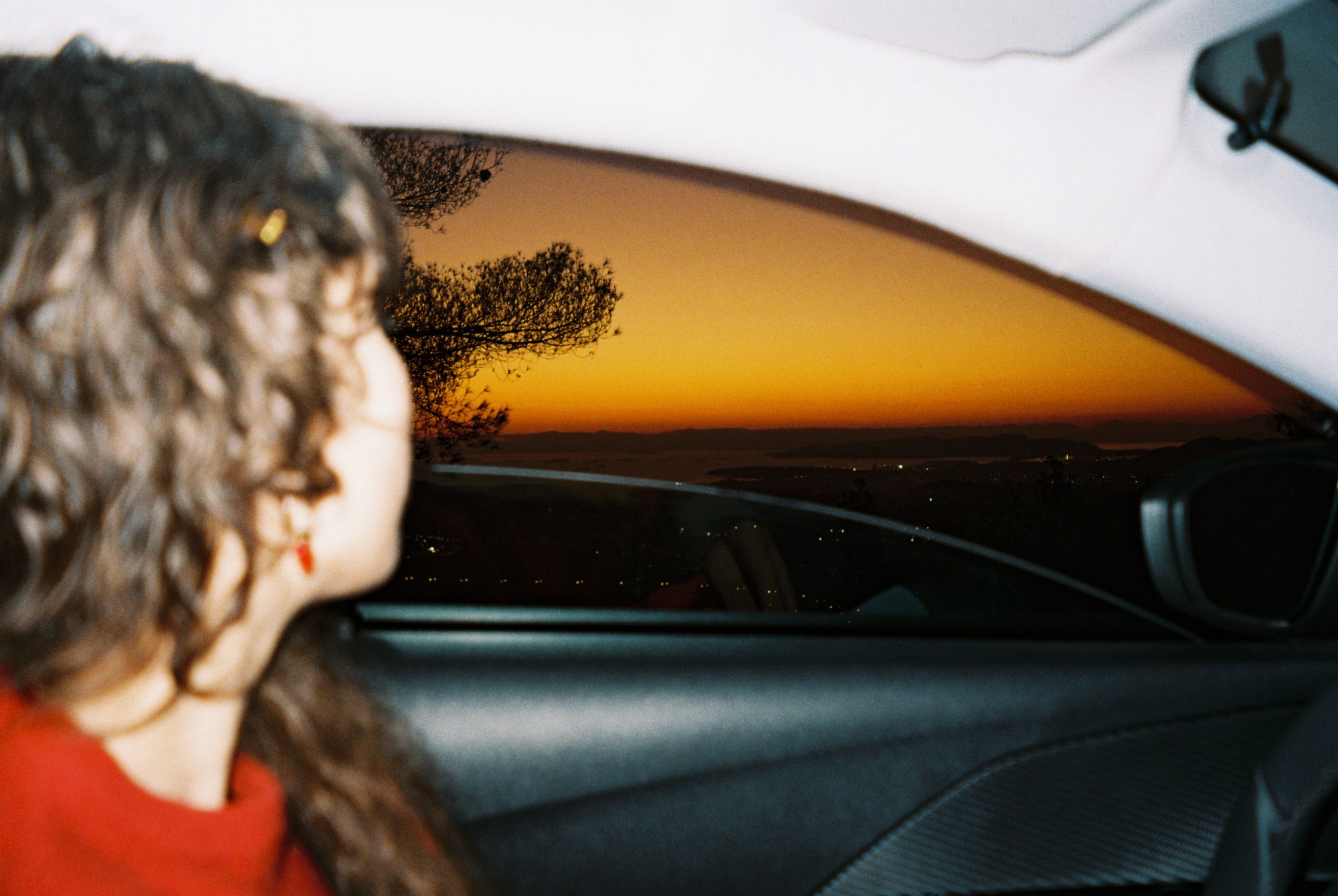 Photograph of a girl looking out the window of a car at sunset.