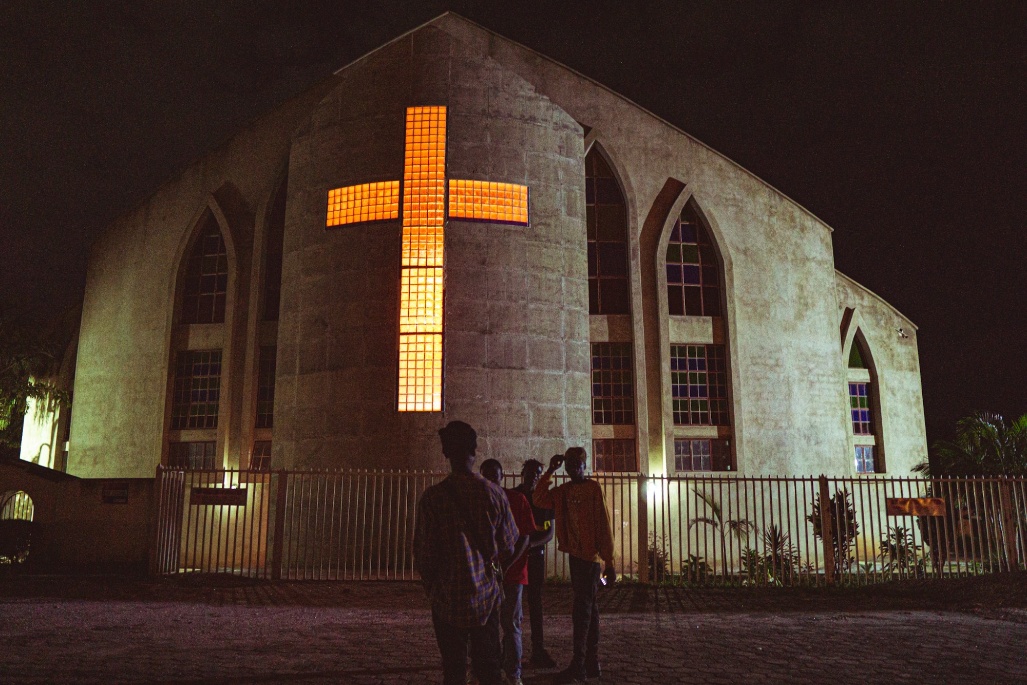 Photograph of a crucifix window in a church lit from the light inside and four boys standing outside.