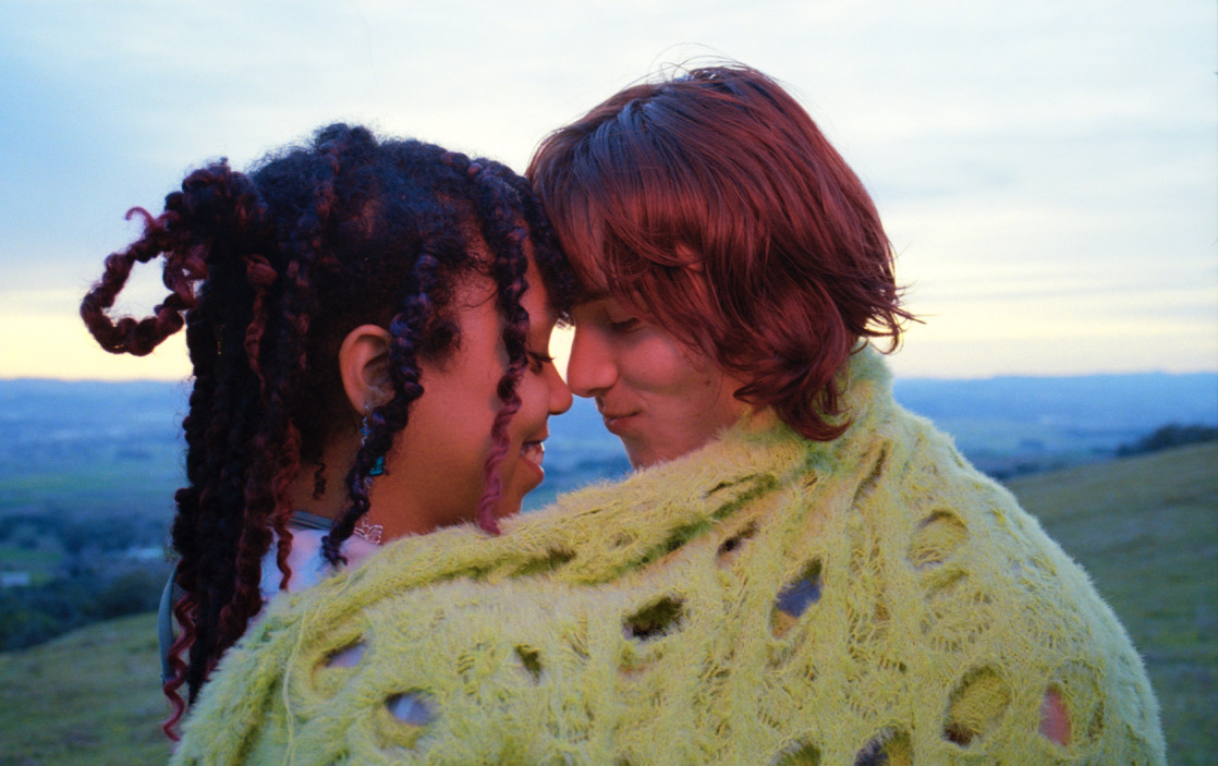 Photograph of two friends wrapped in a blanket with their heads close together intimately.