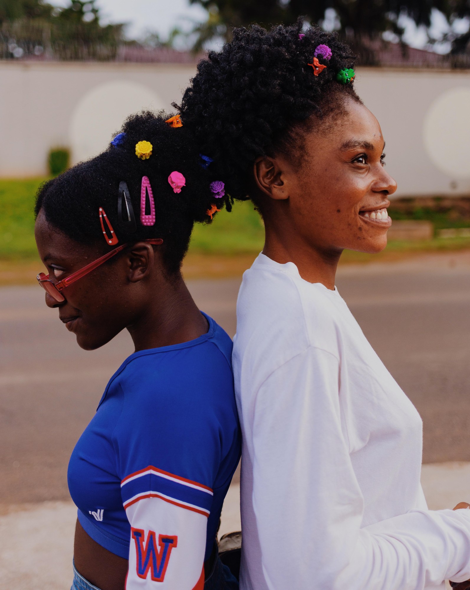 Photograph of two girls with clips in their hair sitting back-to-back and smiling.