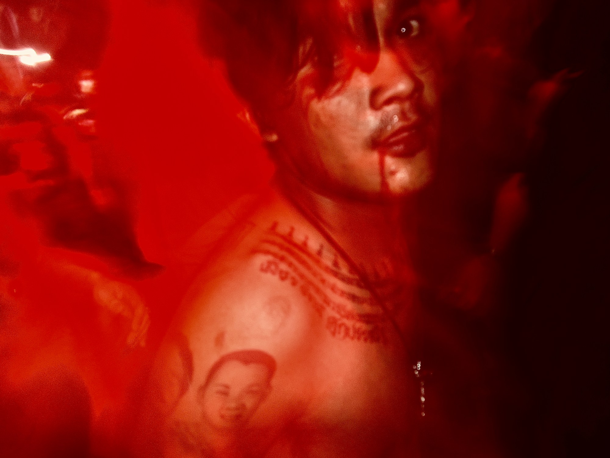 Photograph of a shirtless man covered in tattoos and red paint on his face dancing at a concert