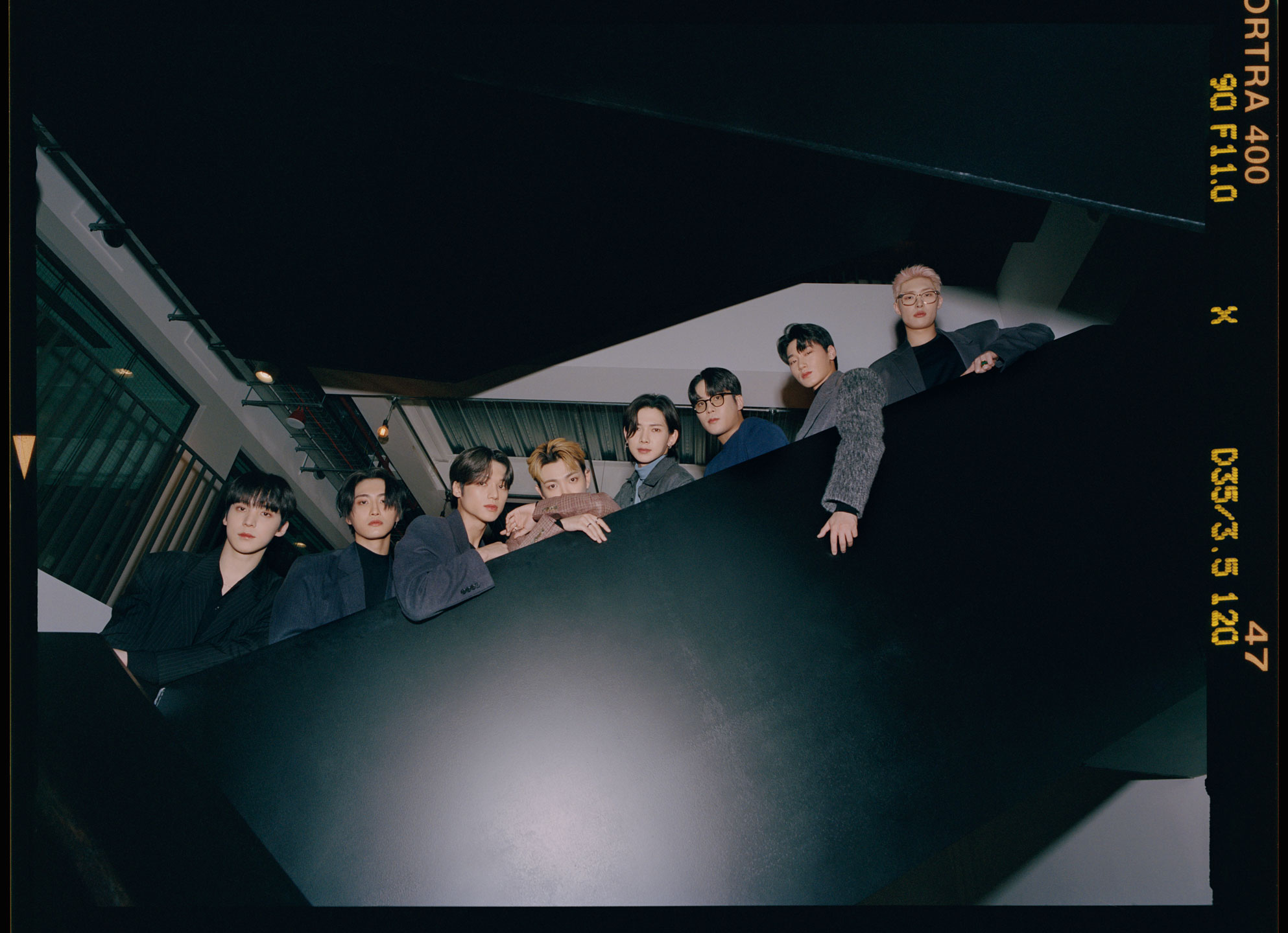 the k-pop group ATEEZ lean over the side of a floating staircase, looking to camera