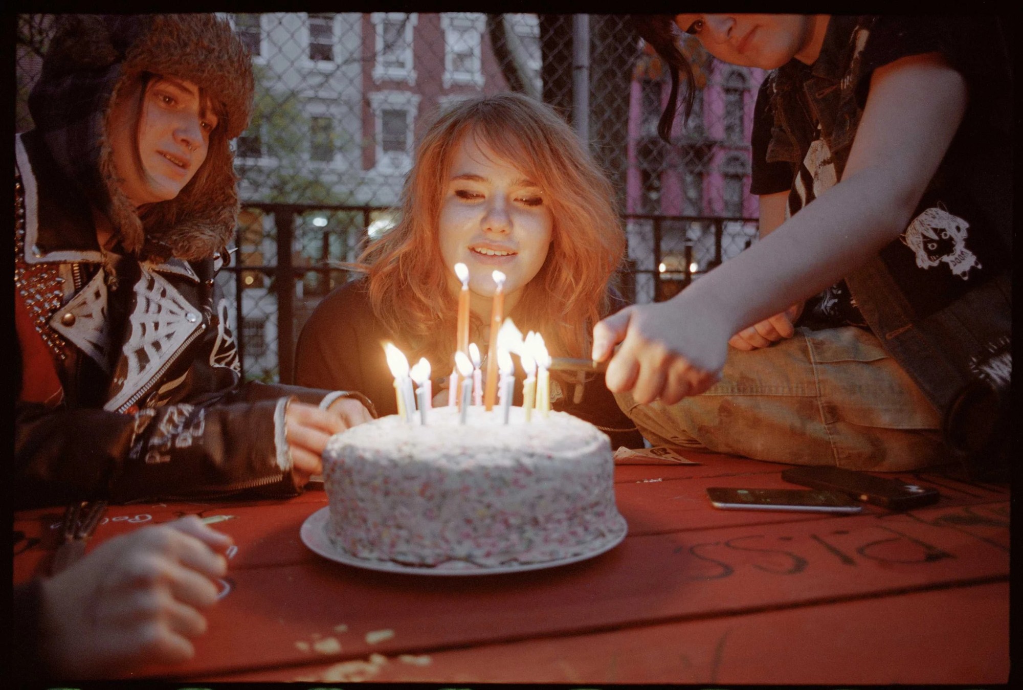 three teenagers sit around a birthday cake lit with candles