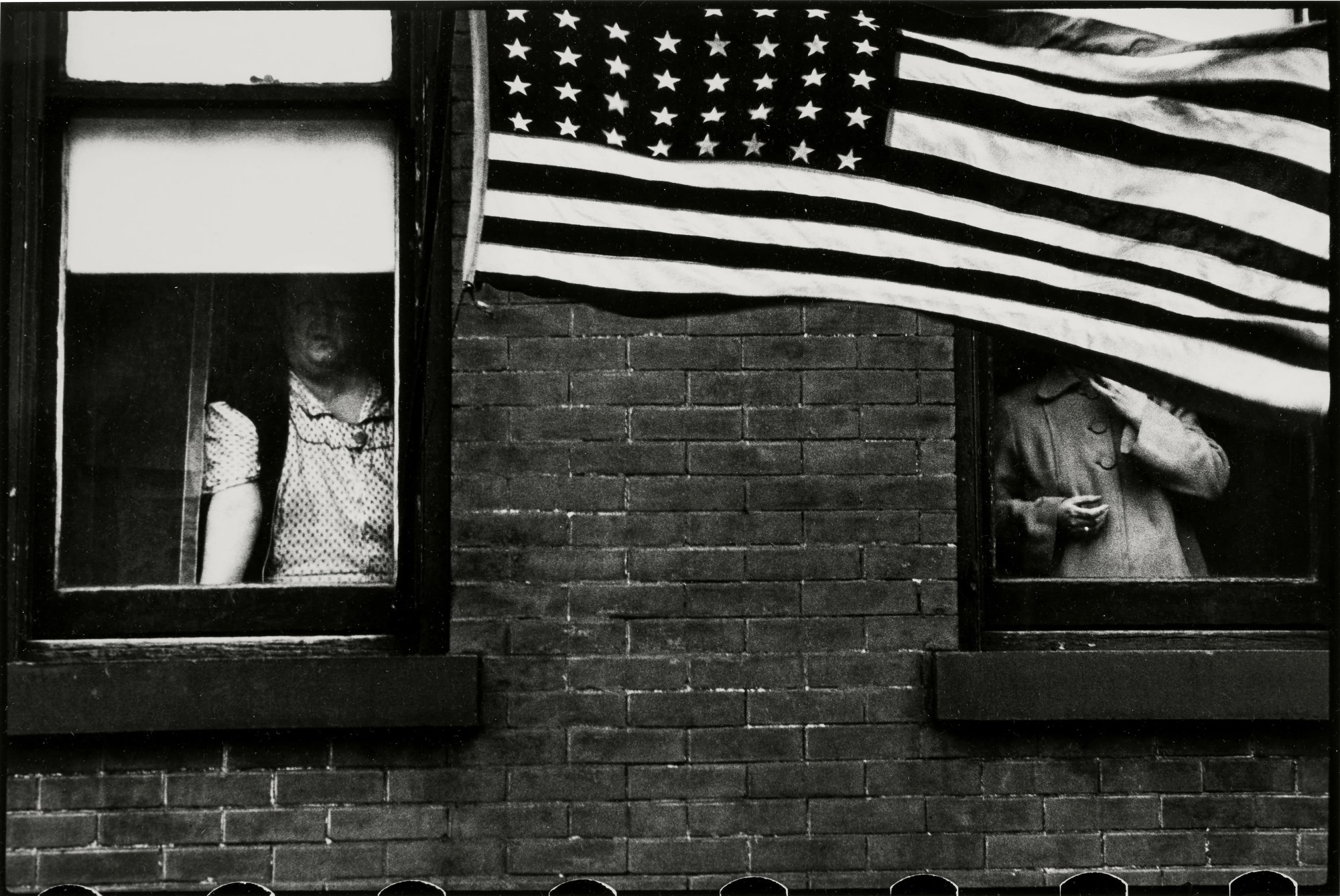 two windows with people stood behind them, an american flag connects them