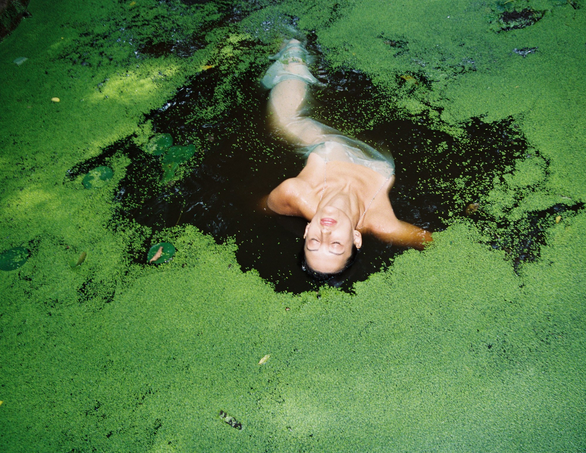 A woman swimming in a mossy lake.