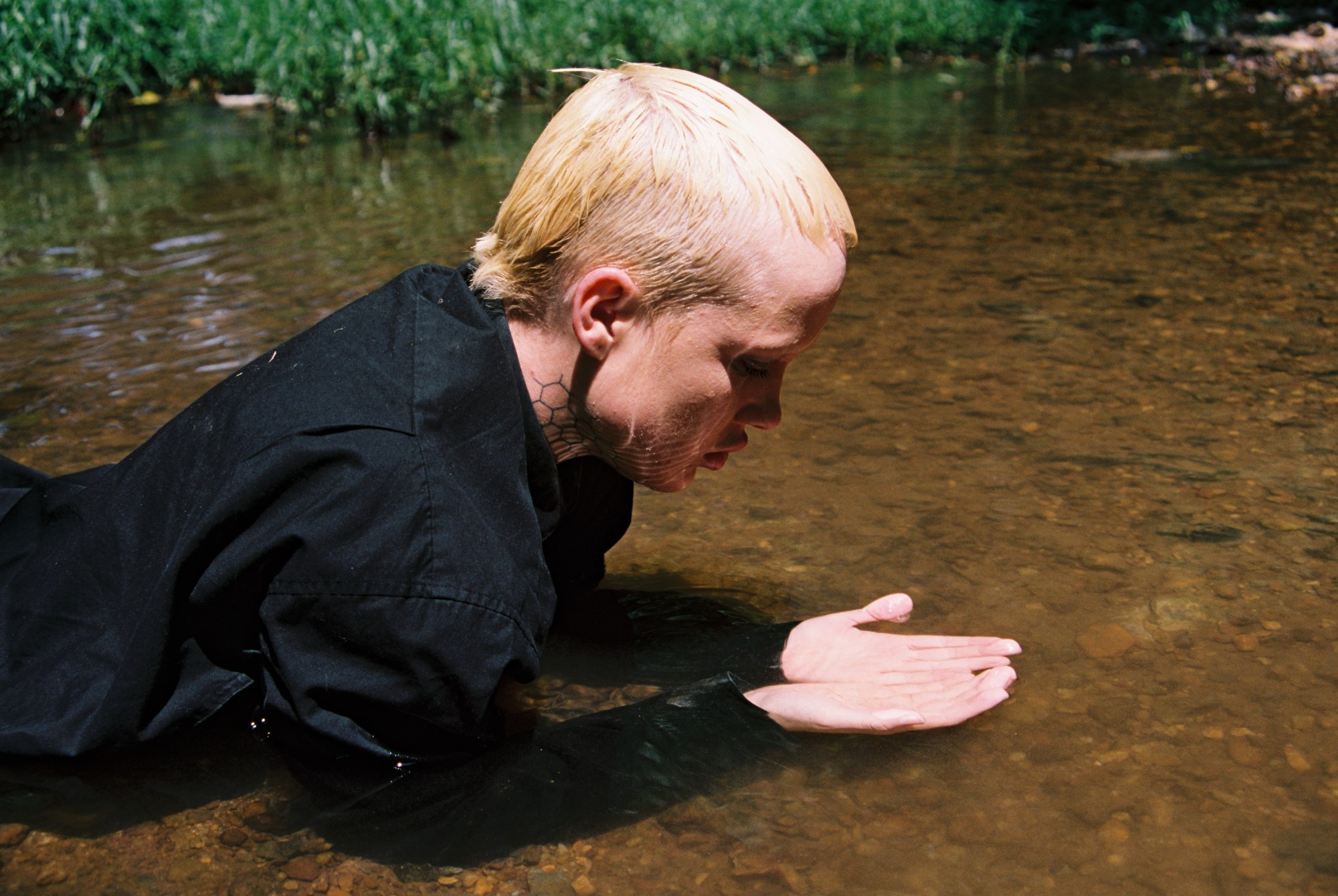 A young person looking at their hands while wearing all black submerged in a shallow pool of water