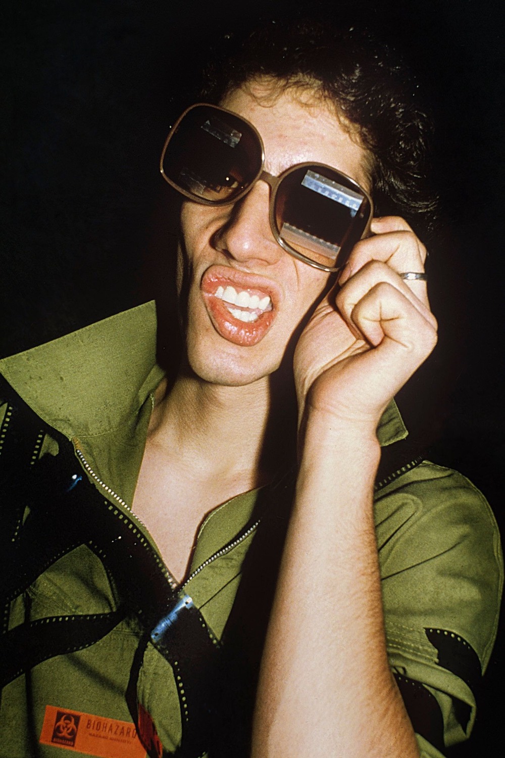 a man holds large sunglasses over his eyes wearing a green jumpsuit