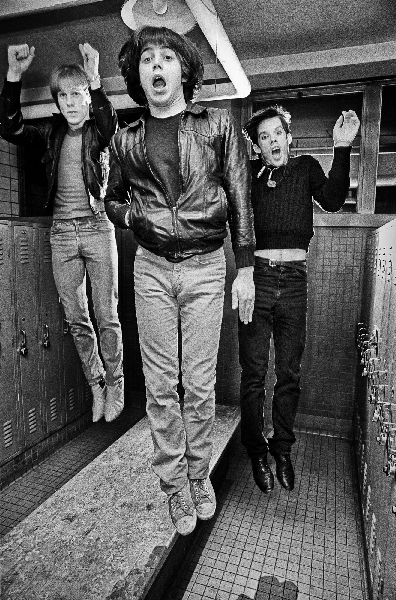 a trio band in a locker room dressed in 70s street style all jumping simultaneously