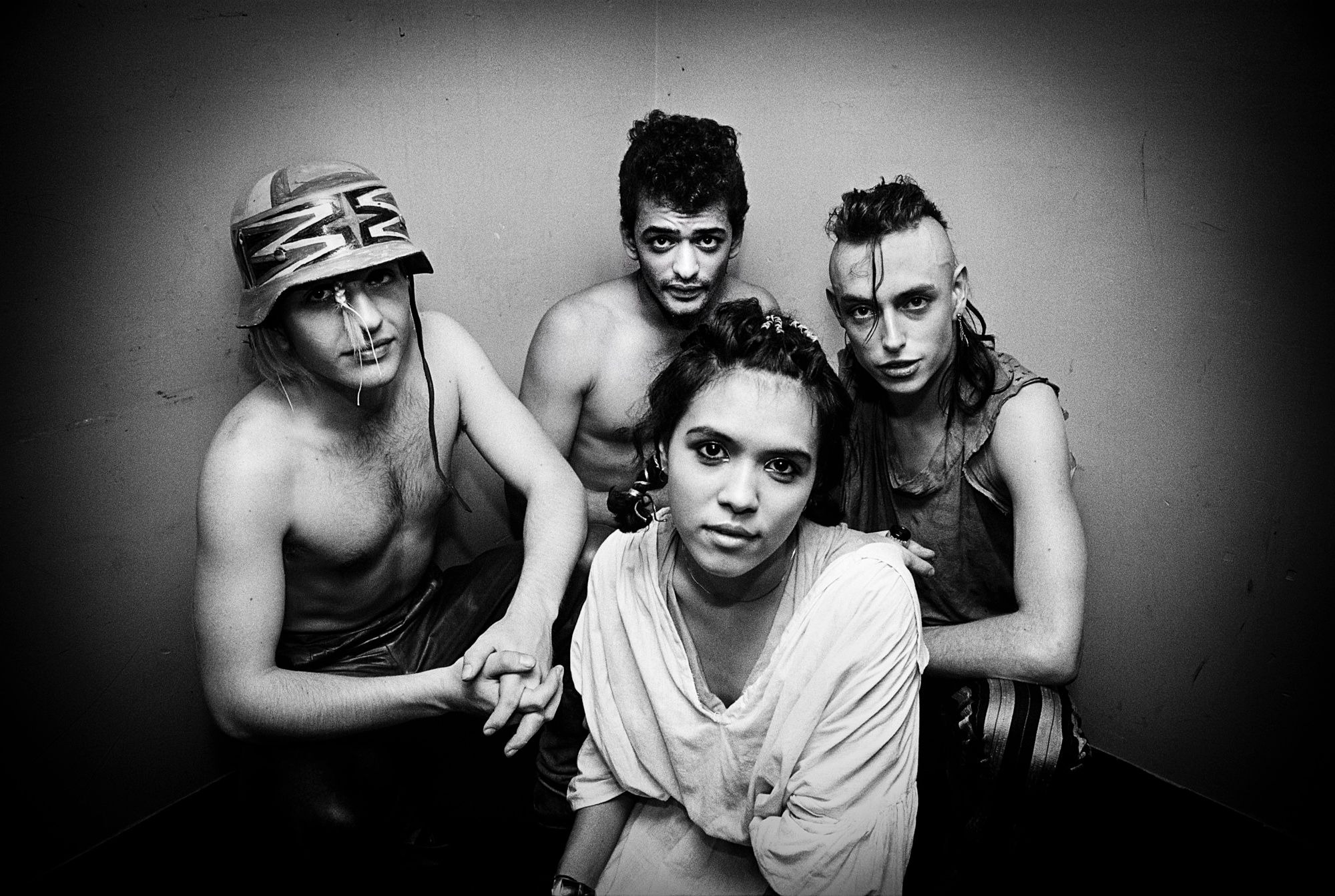 a band with four members, bow wow wow, pose for a portrait against a black background. they're wearing militiary helmets, torn shirts and vests