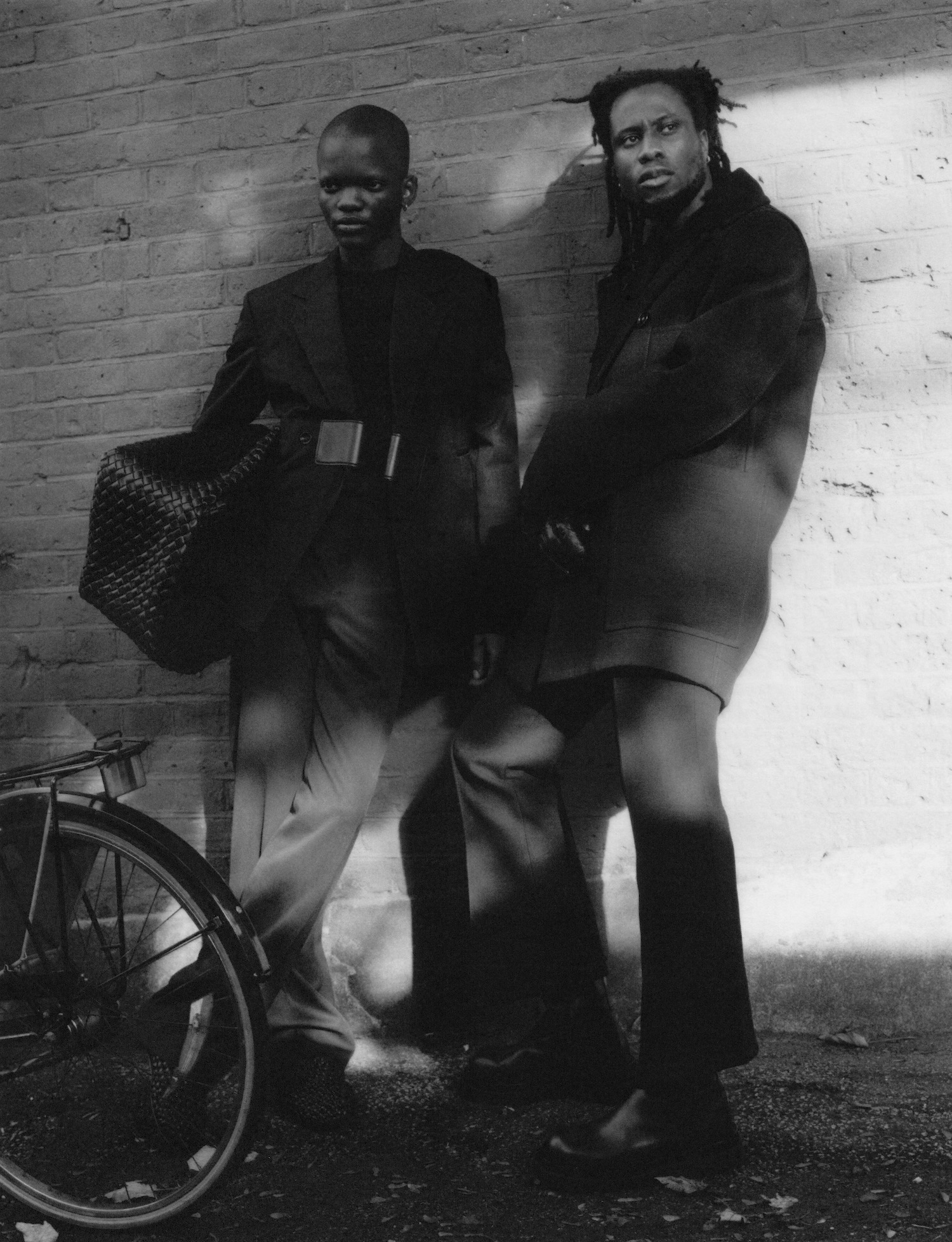 Two men posing in all black in front of a wall