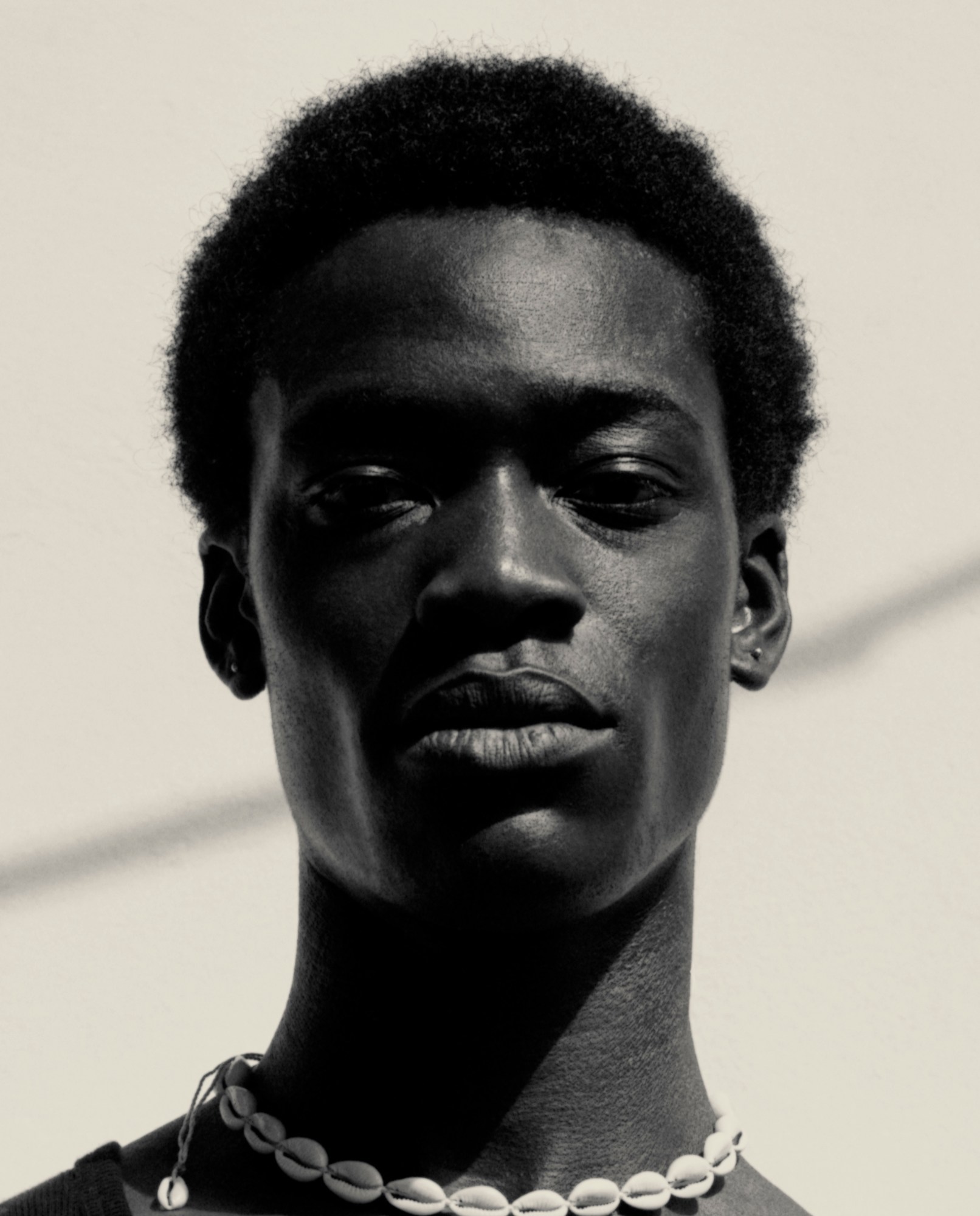 A young man in a shell necklace posing for a black and white portrait