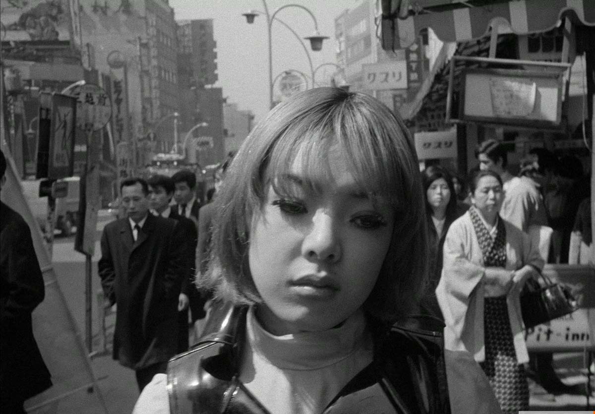 Black-and-white image of a woman with short hair and bangs walking on the crowded streets of Japan