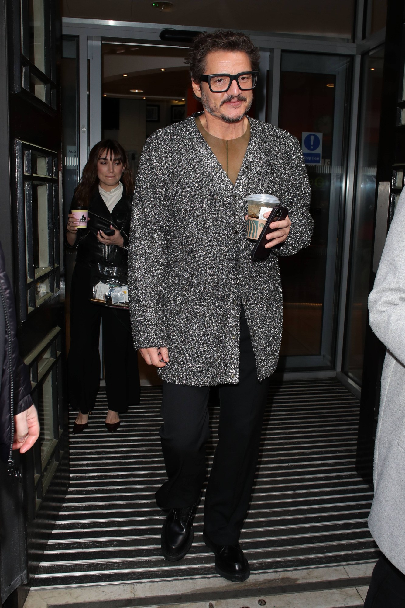 Pedro Pascal leaving a building in a silver knit cardigan holding a starbucks drink in London in 2023