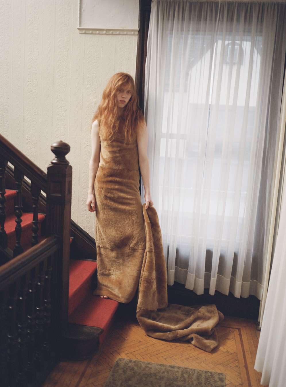 Model standing on the stairs by a window wears dress by Ponte in a photograph by Deirdre Lewis in i-D’s The Timeless Issue, no. 371, Spring 2023