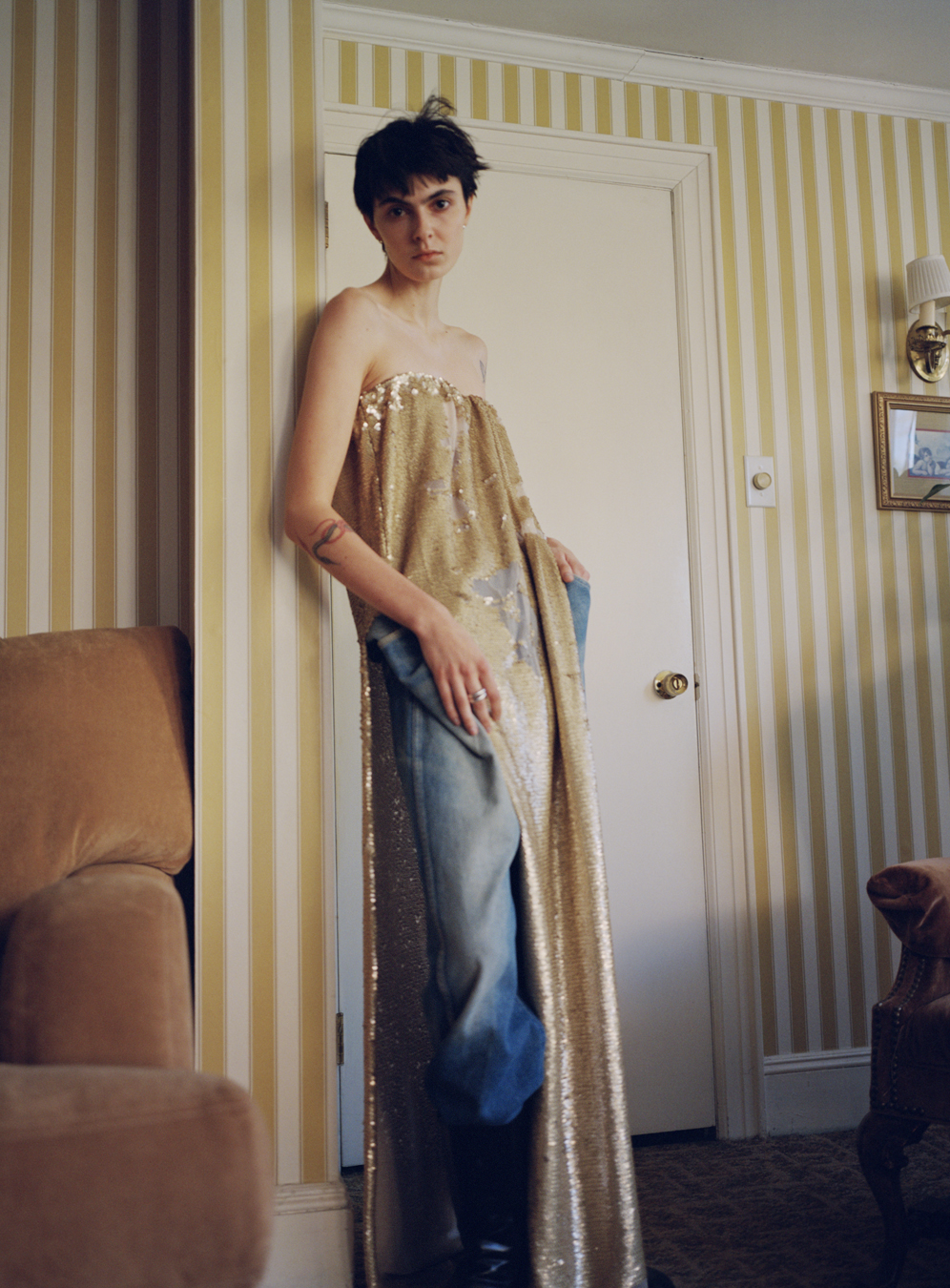 Model standing in a living room wears dress and jeans by Ponte in a photograph by Deirdre Lewis in i-D’s The Timeless Issue, no. 371, Spring 2023