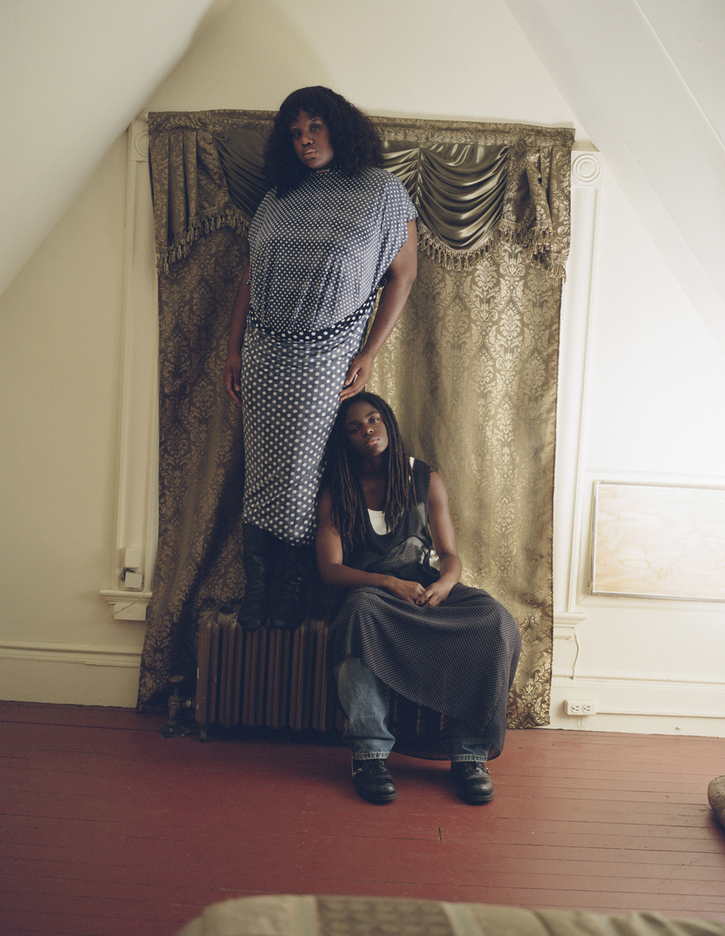 Two models sitting and standing on a radiator wear clothes by Ponte in a photograph by Deirdre Lewis in i-D’s The Timeless Issue, no. 371, Spring 2023