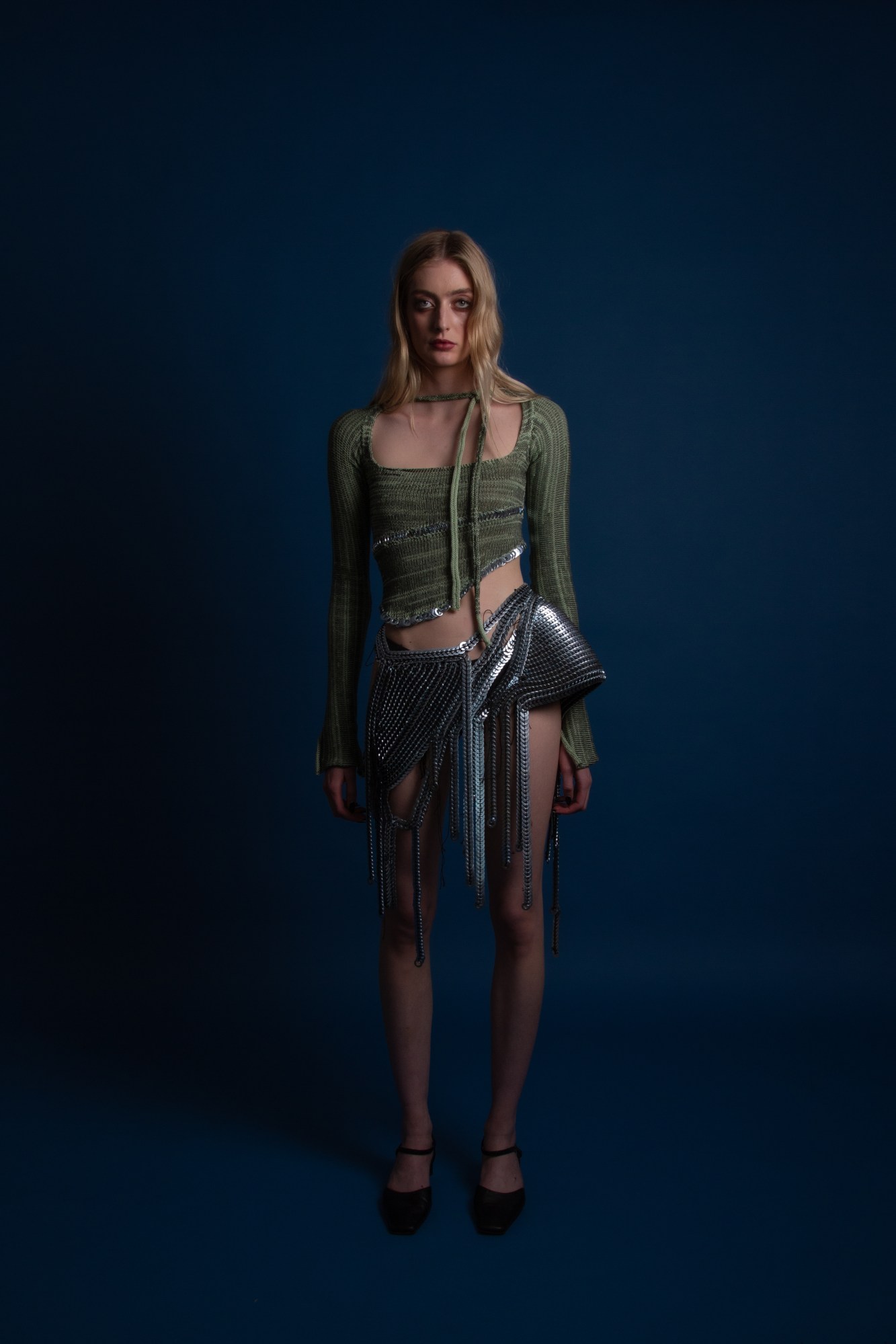 a model posing in a chainmail skirt and knit sweater by mega mikaela