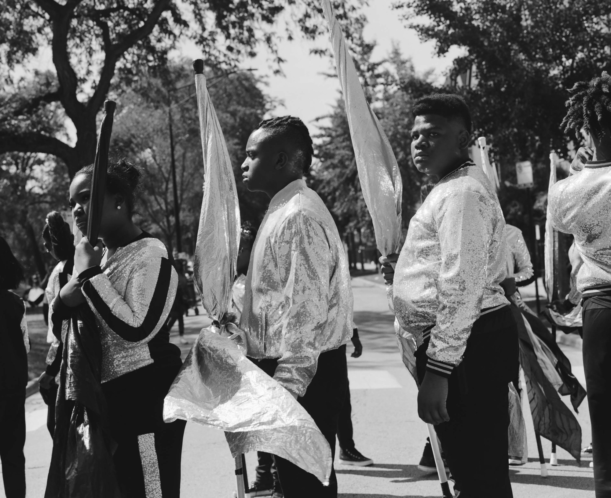 Black-and-white photo of young people in in Chicago's South Shore Drill Team wearing sparkly zip up jackets and carrying flags