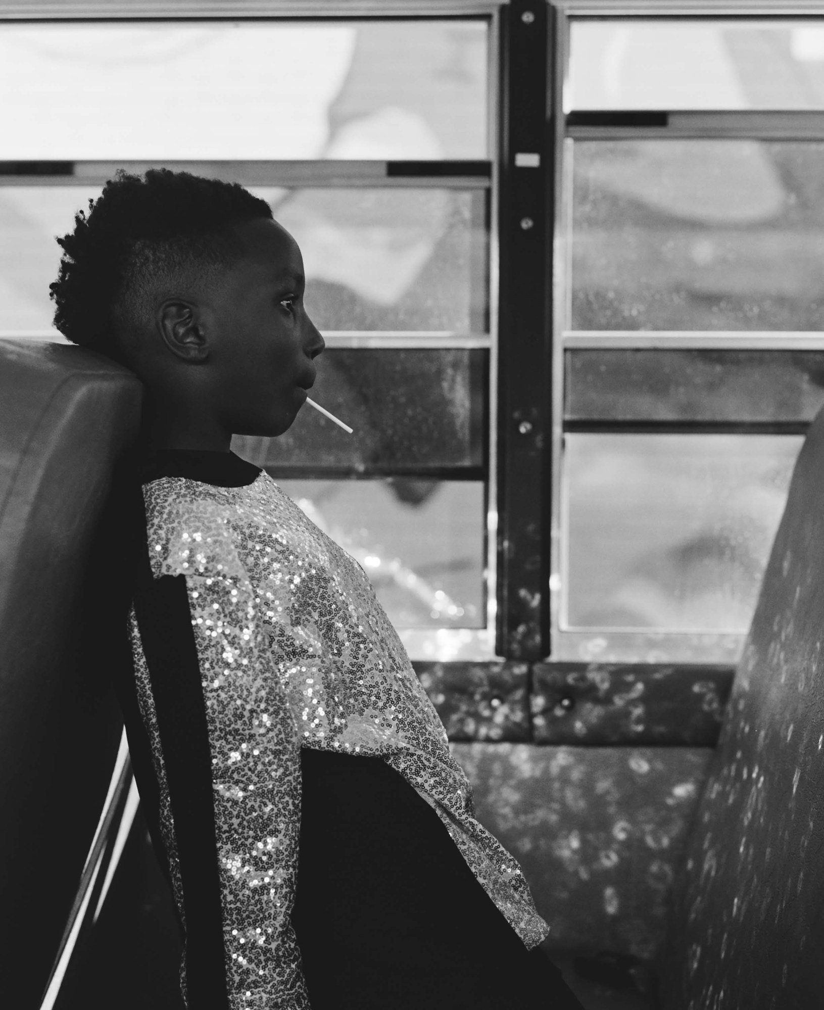 Black-and-white photo of a young member of Chicago's South Shore Drill Team in sparkly top sitting on a bus