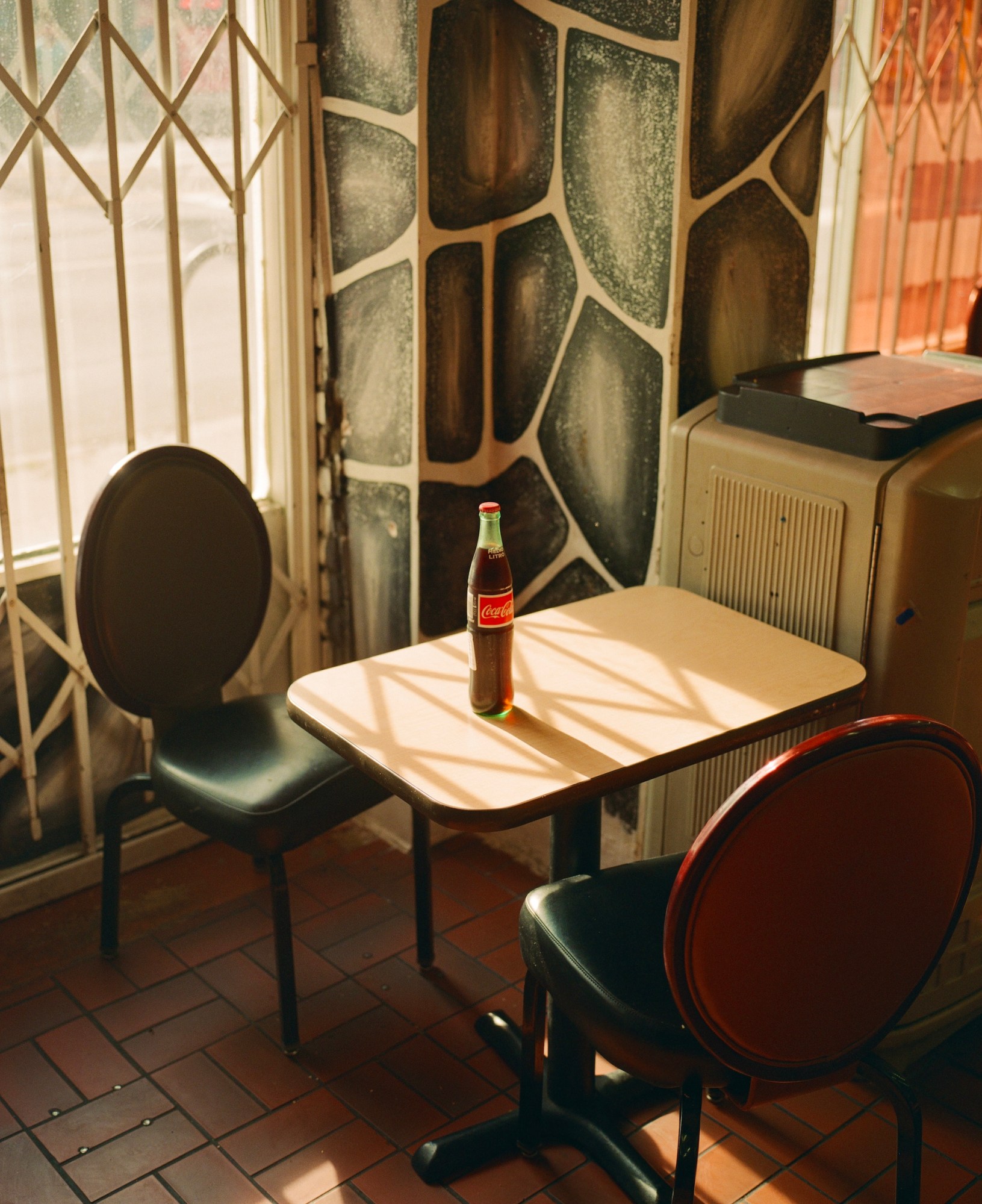 a coke bottle sitting on a diner table with vinyl chairs