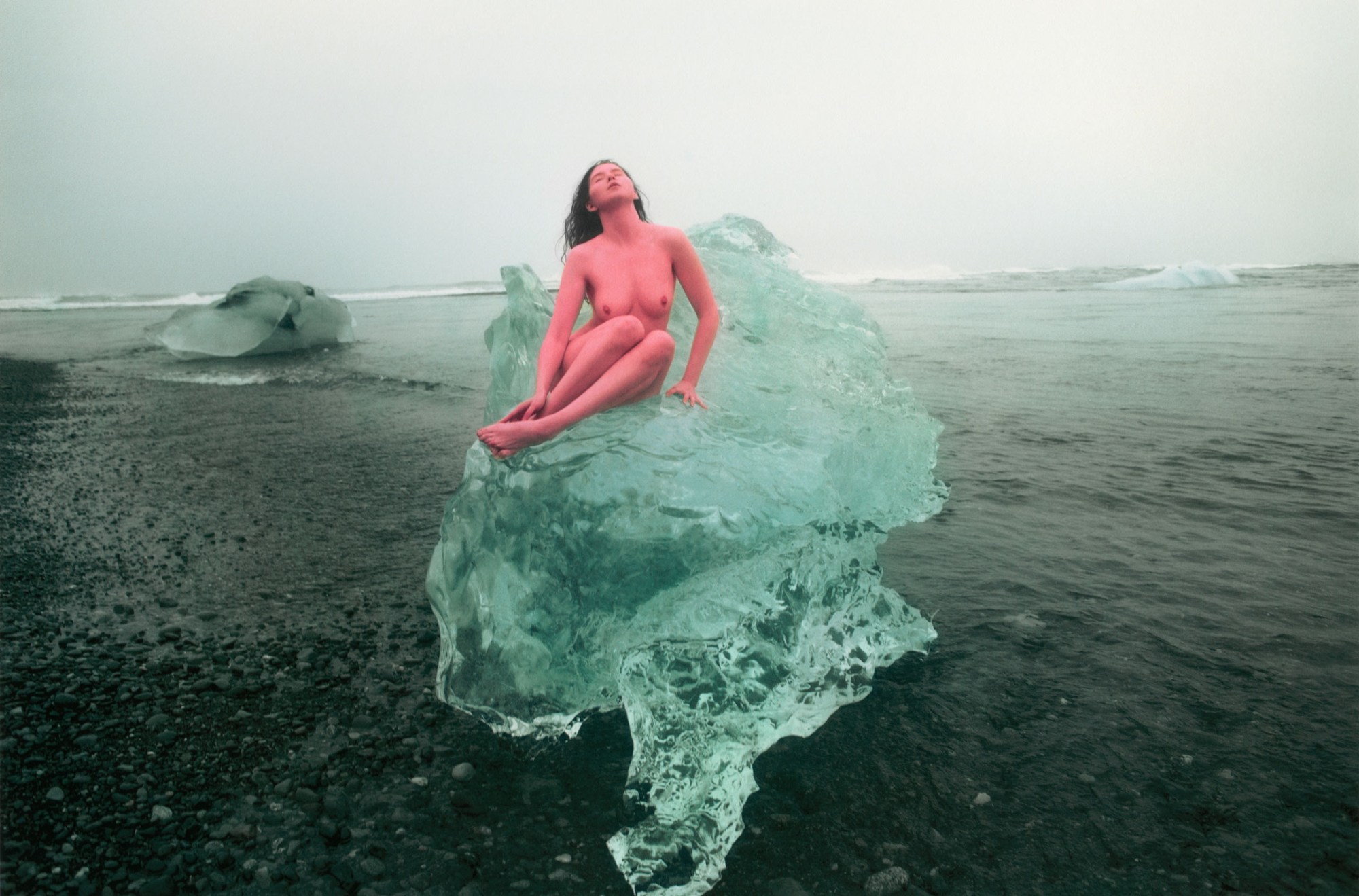 a woman (painted pink) sits like a mermaid on an icy structure