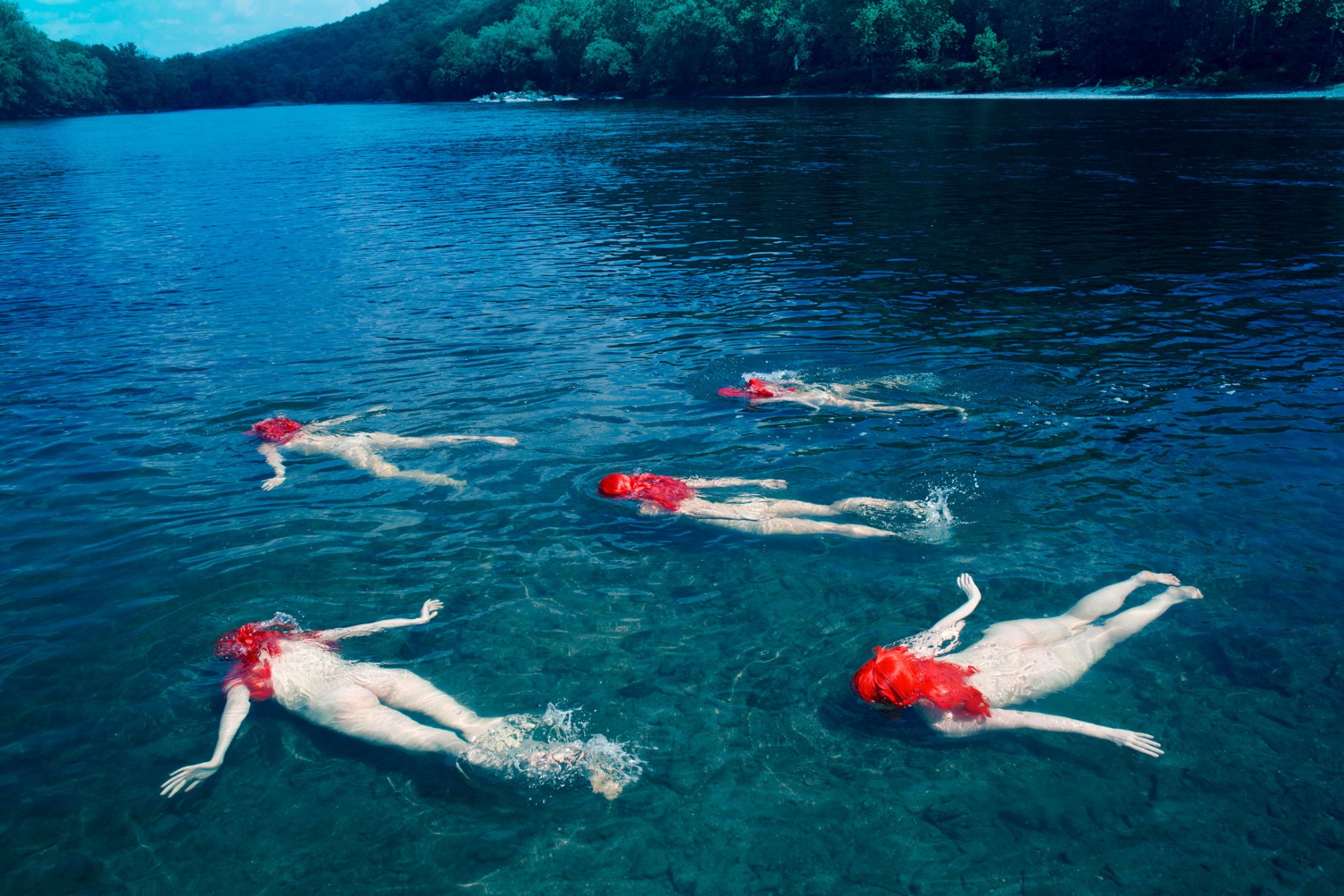 five women with red-painted hair float nude in a calm lake