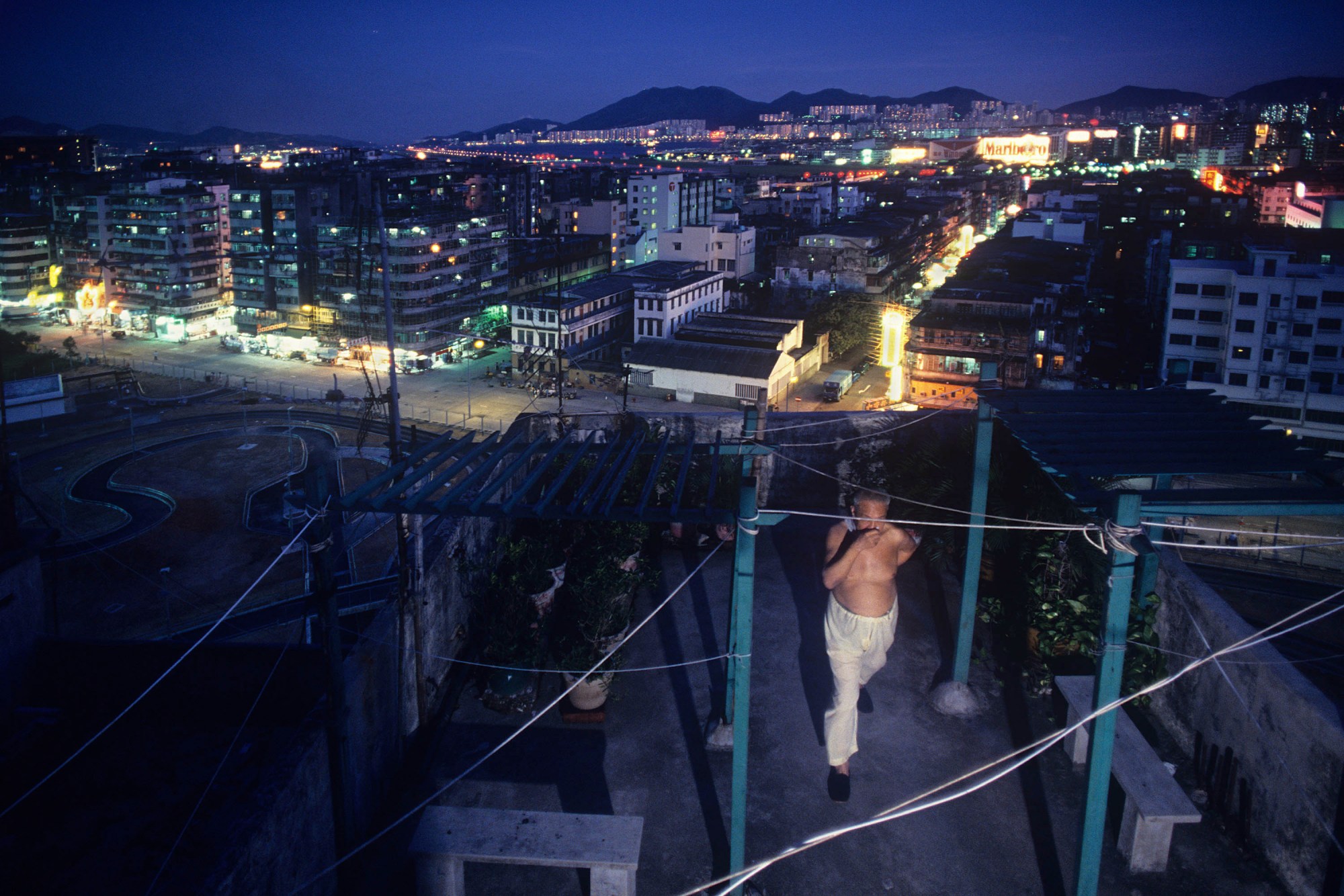 A topless man stands on the roof of Kowloon Walled City at night