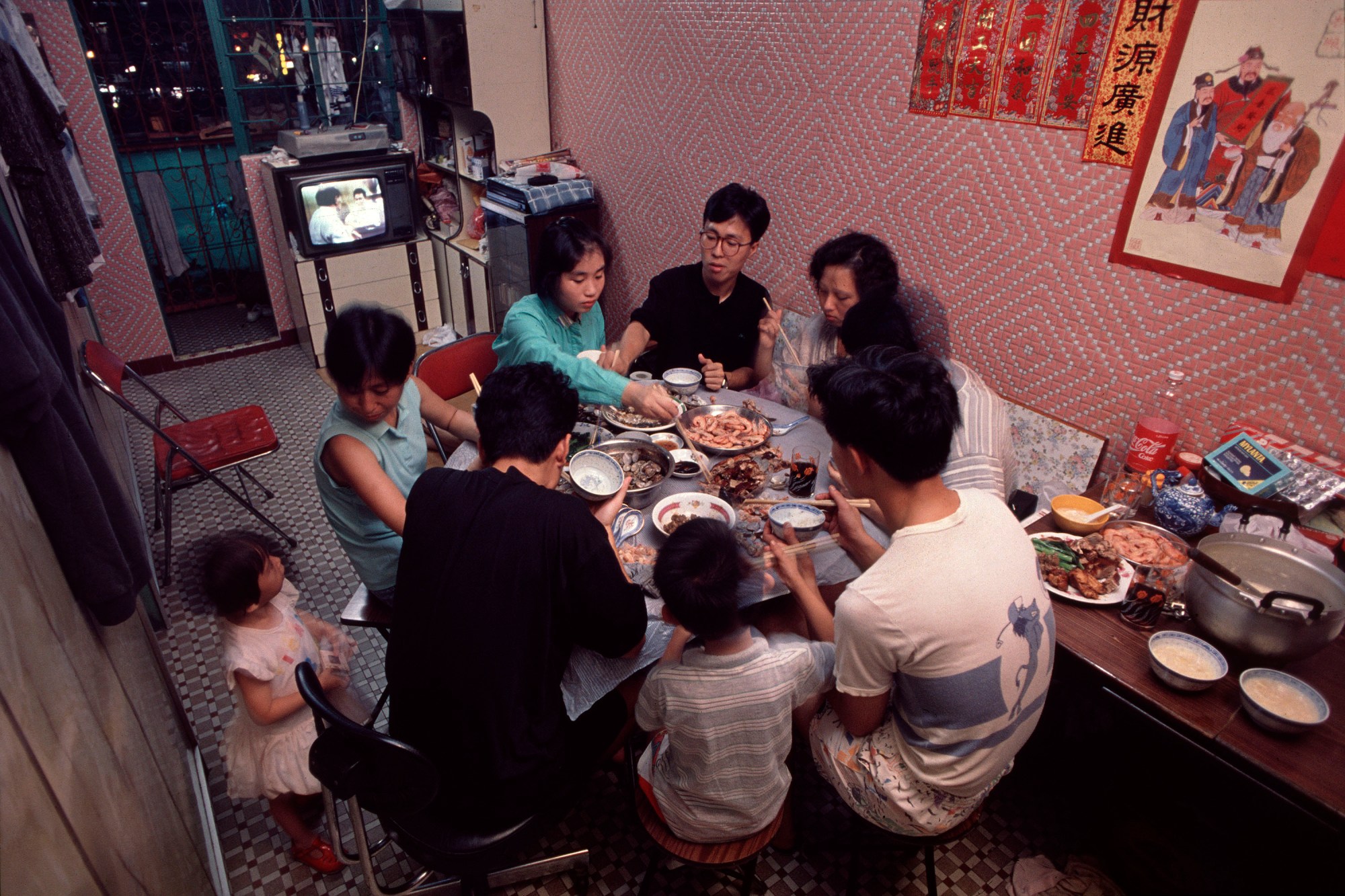 A family gather in a small pink living room to eat dinner within Kowloon Walled City