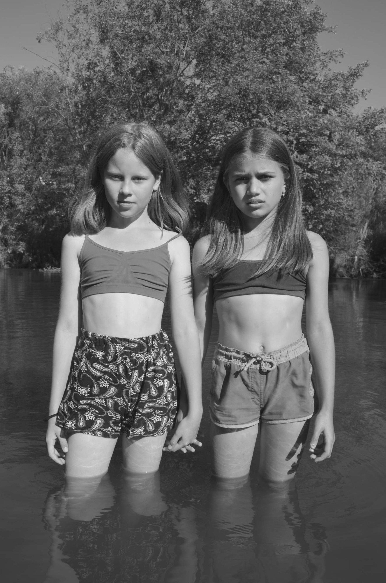 two girls in shorts and training bras hold hands in a lake