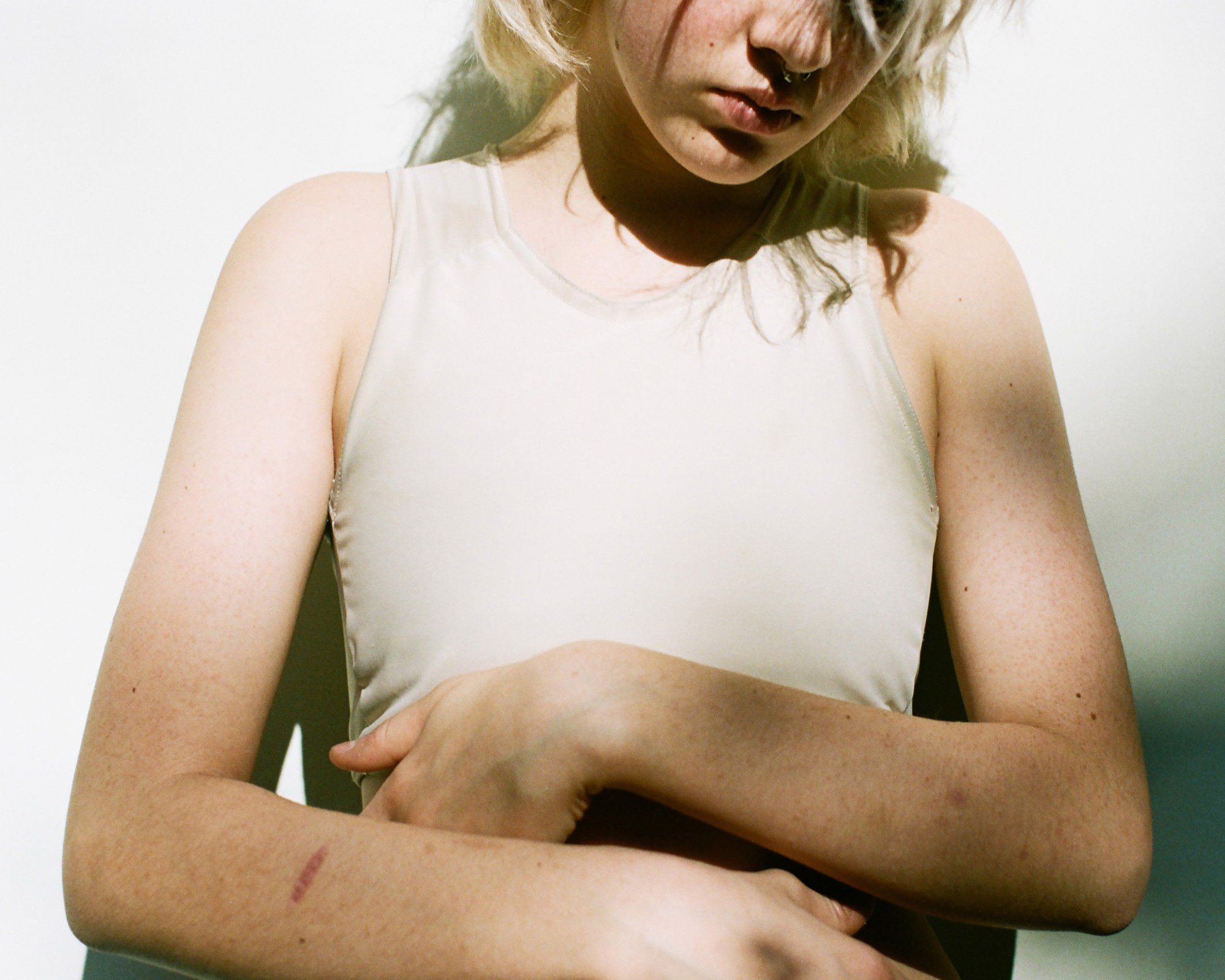 a person with cropped bleach blonde hair wears a binder and stands in the sun