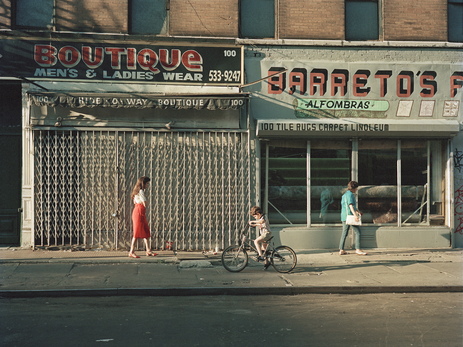 a young boy bikes along a street in front of a shuttered boutique