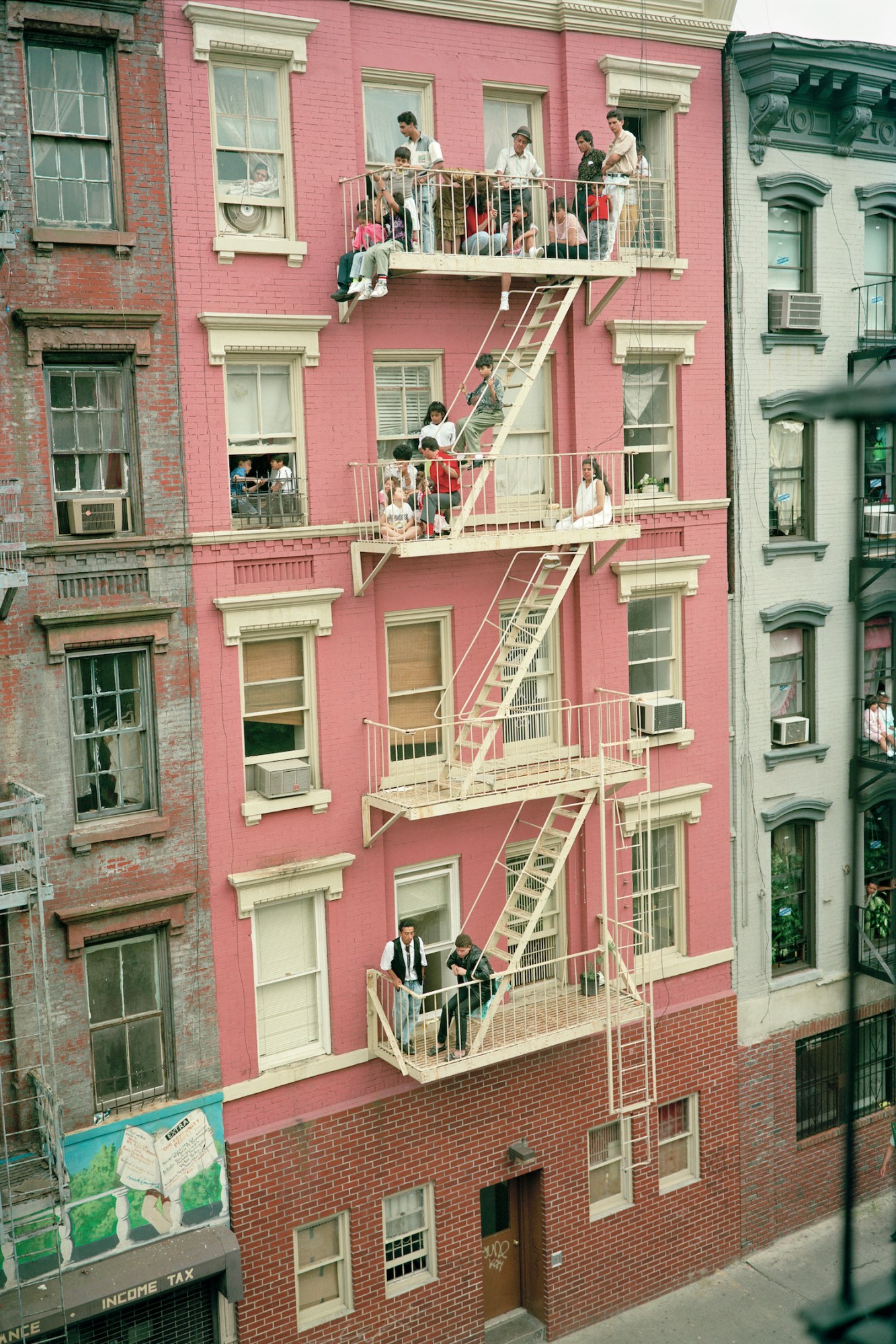 groups of people gather chatting on four levels of fire escape outside a pink painted building