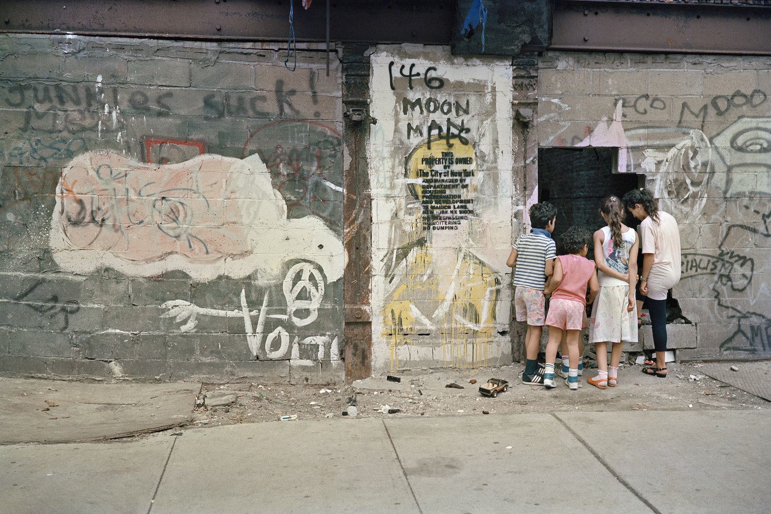 four children gather looking at a poster on a graffitied street