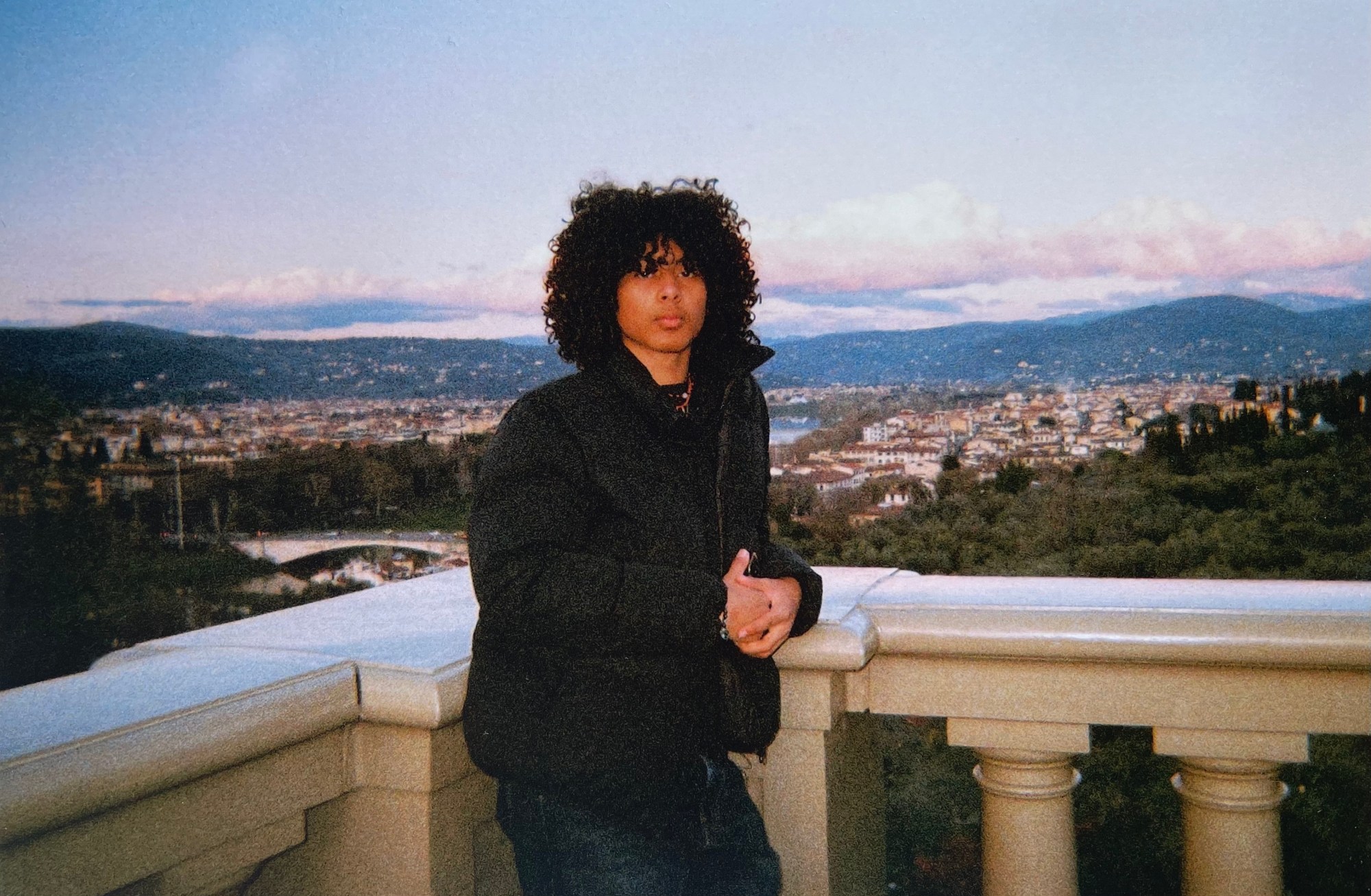 a portrait of the artist daniel santangelo high up on a hillside. he has black curly hair and is wearing a puffer jacket.