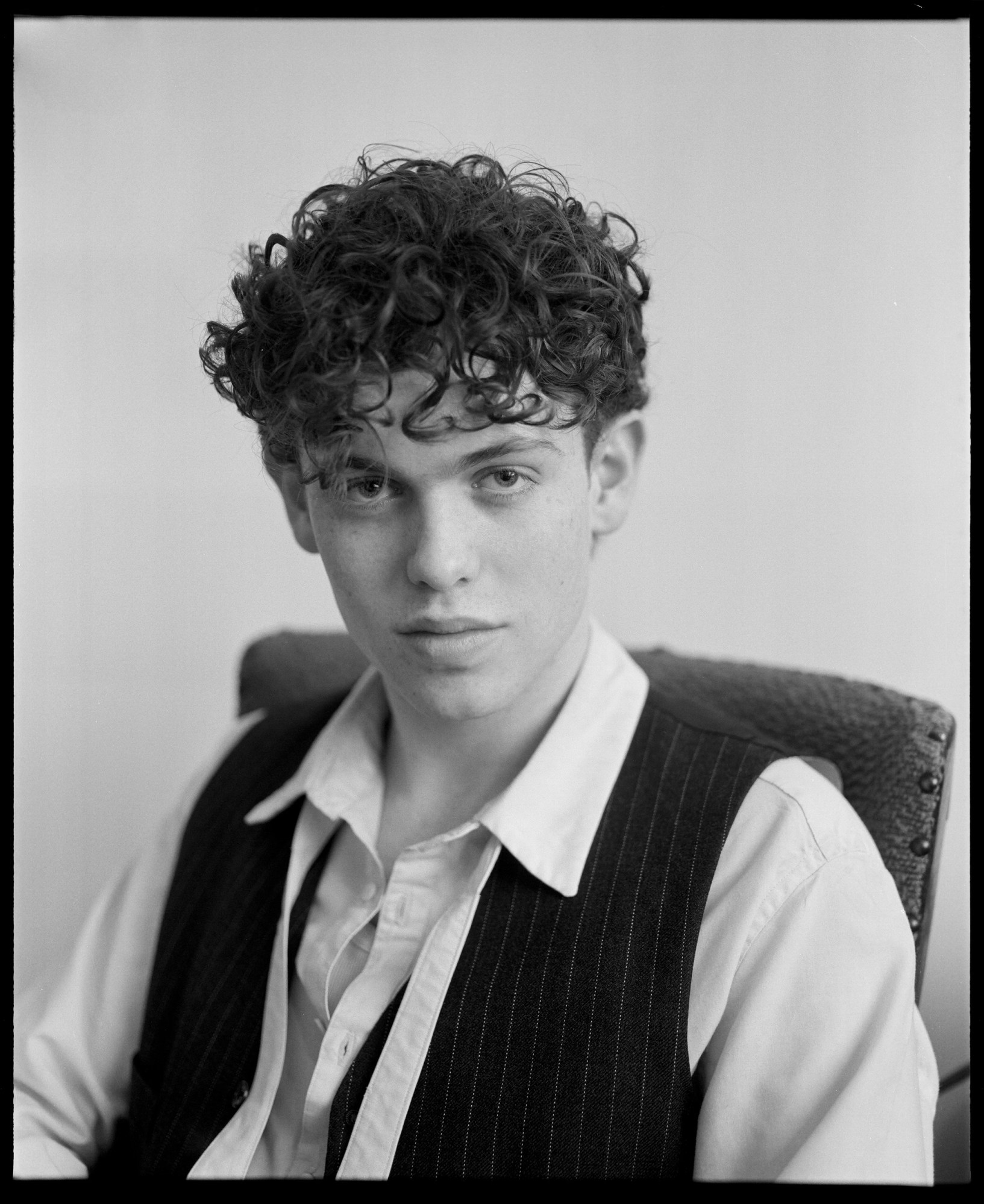 a portrait of designer arthur boyd, wearing a pinstripe waistcoast and shirt . he has short curly hair.