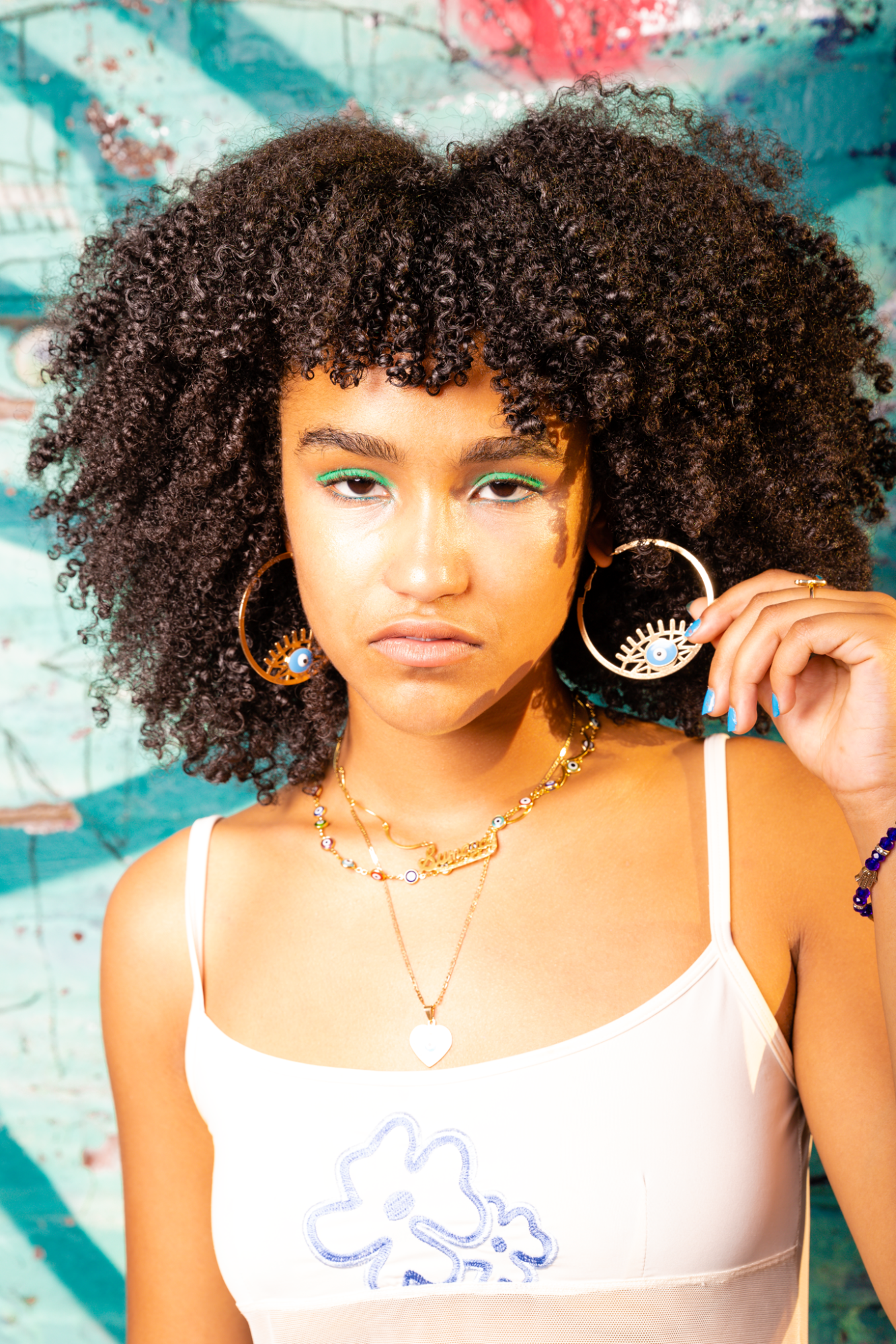 a portrait of the artist musician activist sumaya nazar boubhal wearing a white cropped to. they have curly hair and lurid eye make up.