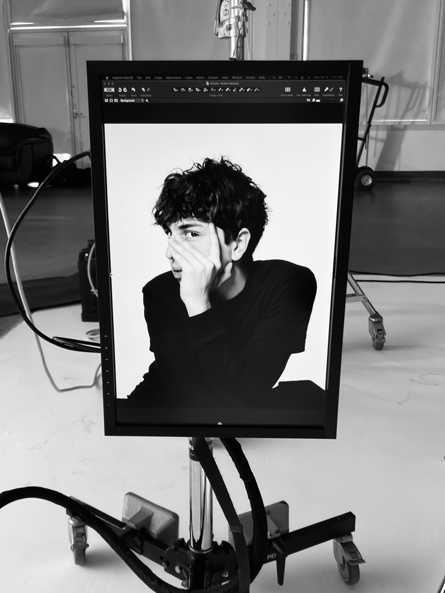 a black and white portrait of the artist nico daniels on a monitor. he wears a black t shirt and has a hand covering his face